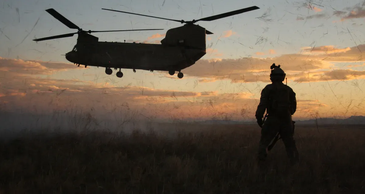 Image of Military member watching as a CH-47 is landing at sunset