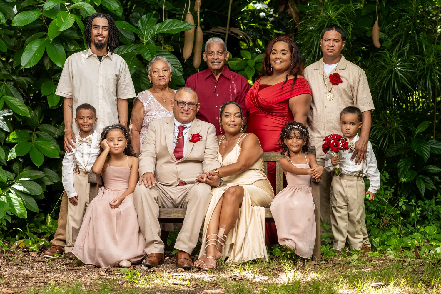 A large family portrait outdoors wearing coordinated cream and burgundy outfits against lush greenery.