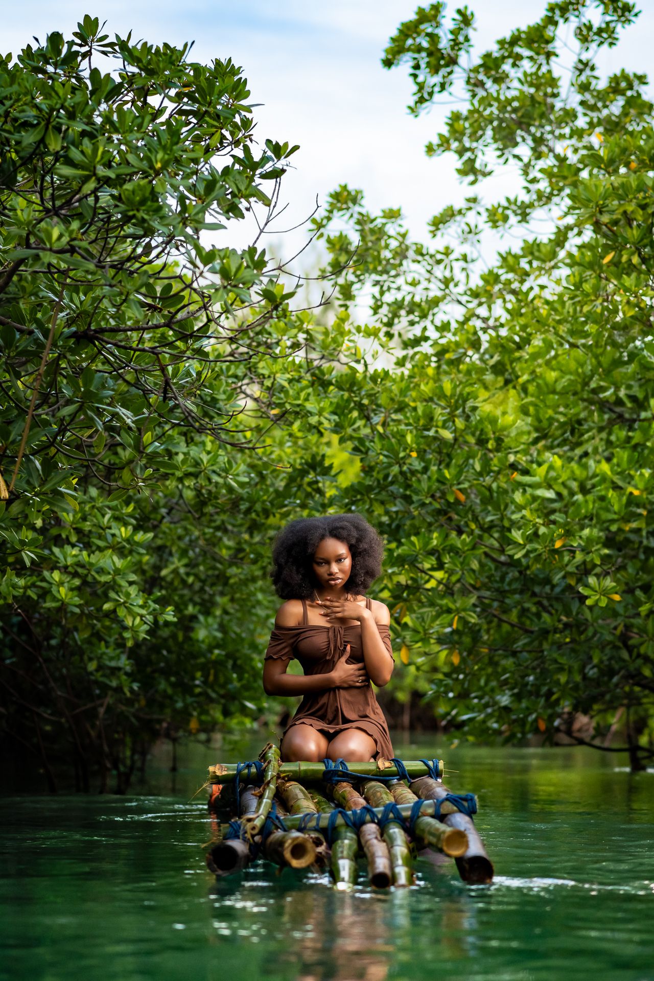 A serene natural scene of someone sitting on a raft floating through mangrove-lined waters in a tropical setting.