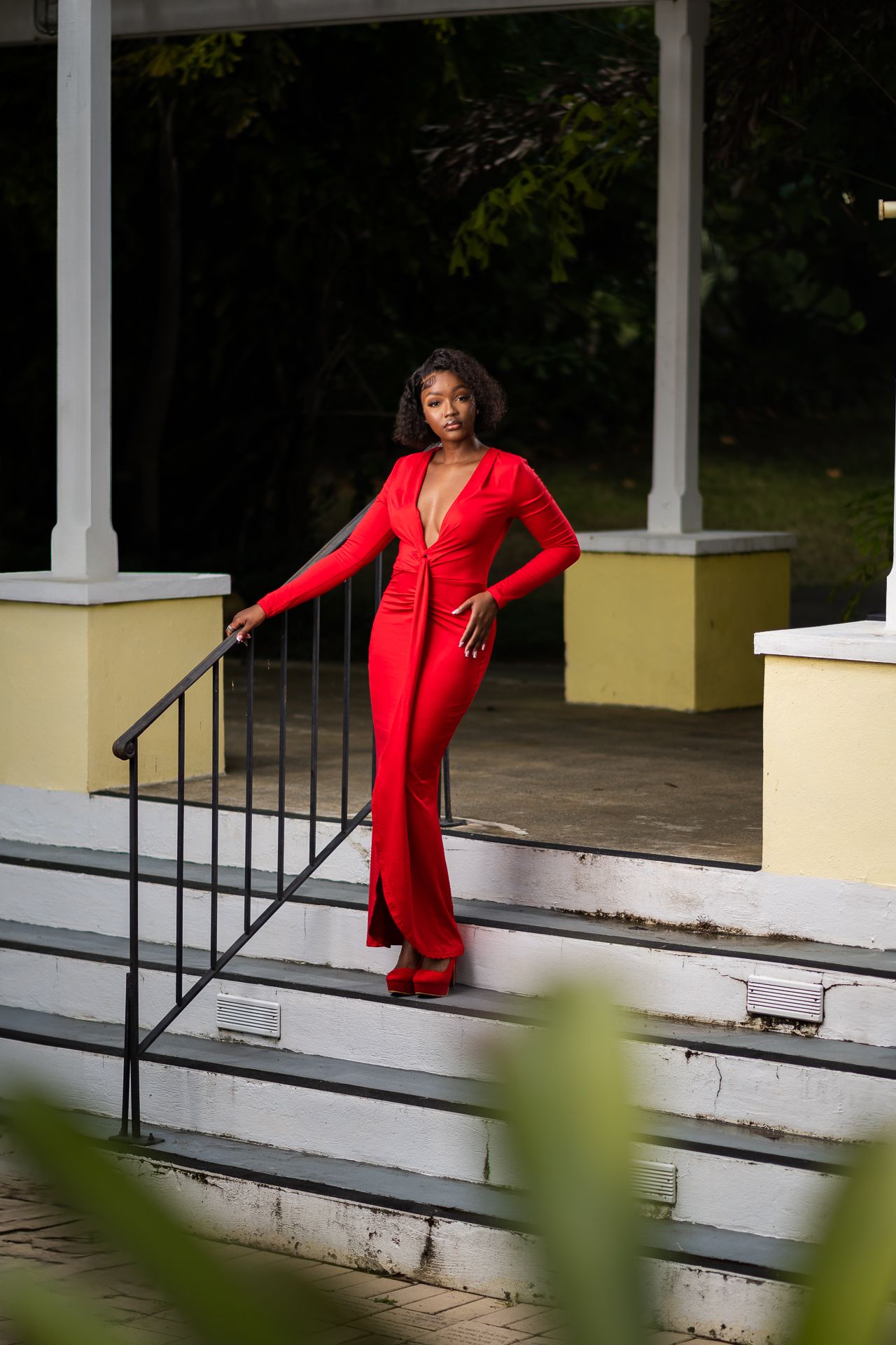 Elegant portrait on white steps wearing fitted red jumpsuit with dramatic neckline.