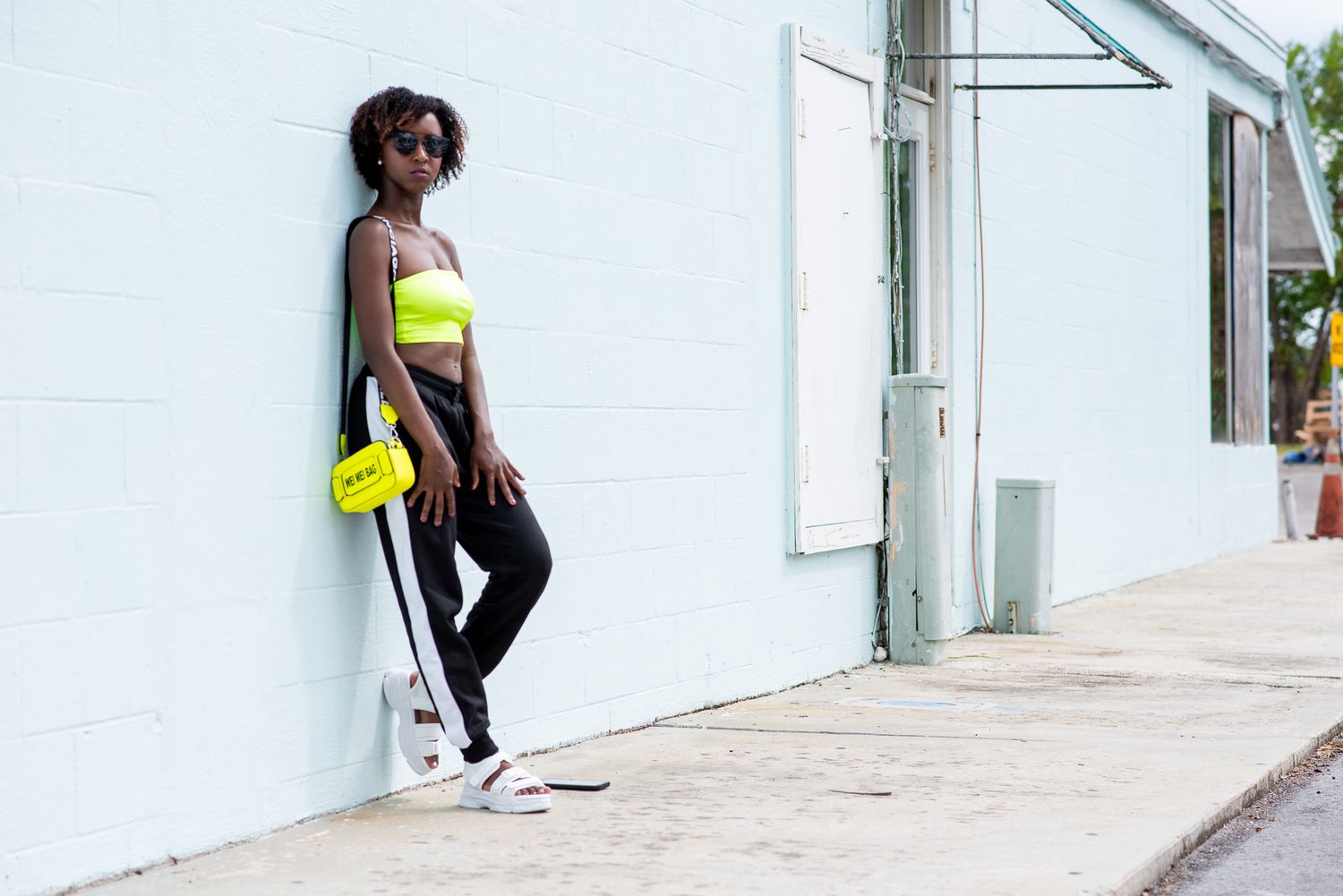 Person in casual attire posing against a white wall in urban setting.