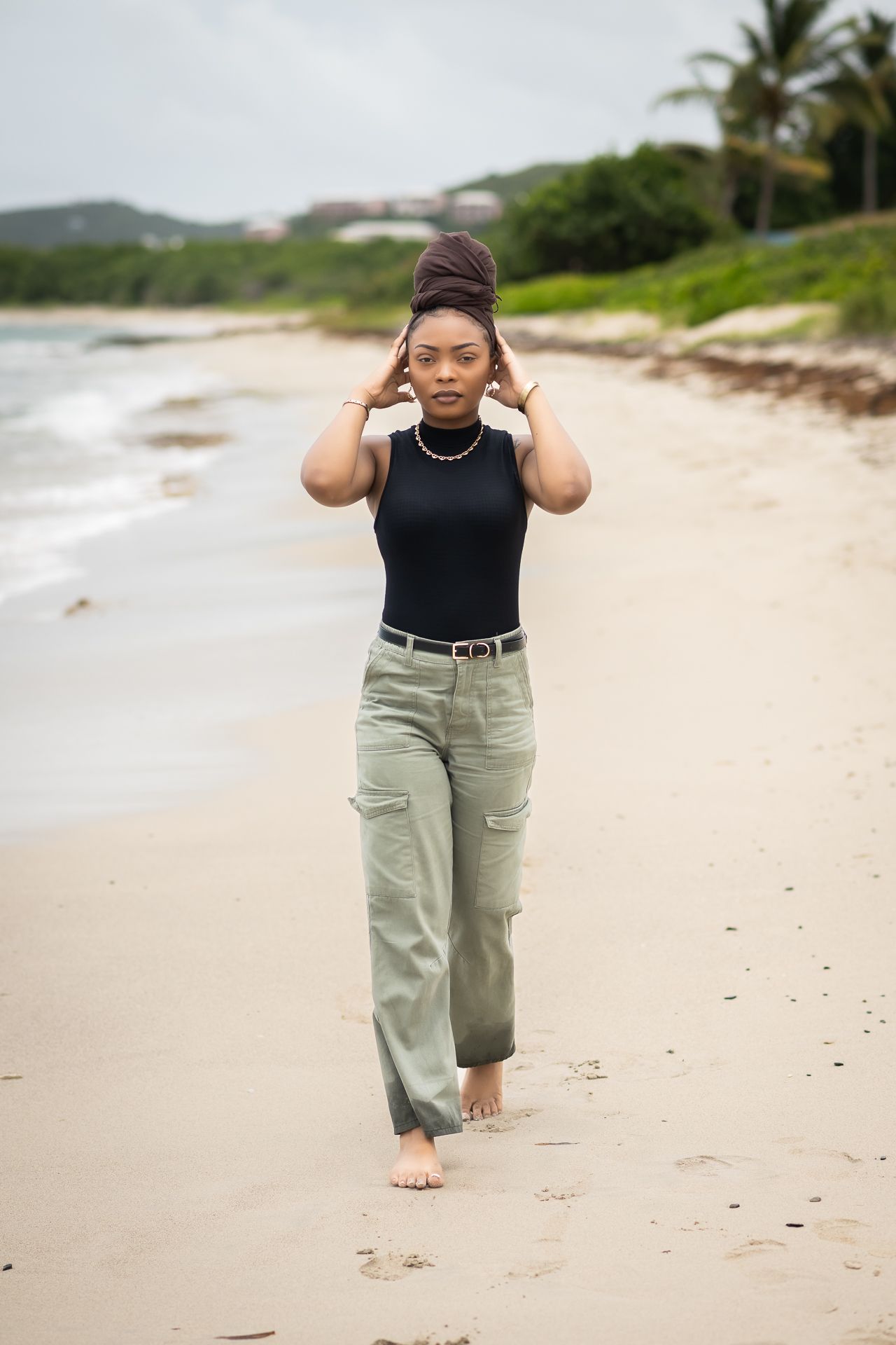Person walking barefoot on beach wearing black top and khaki pants.