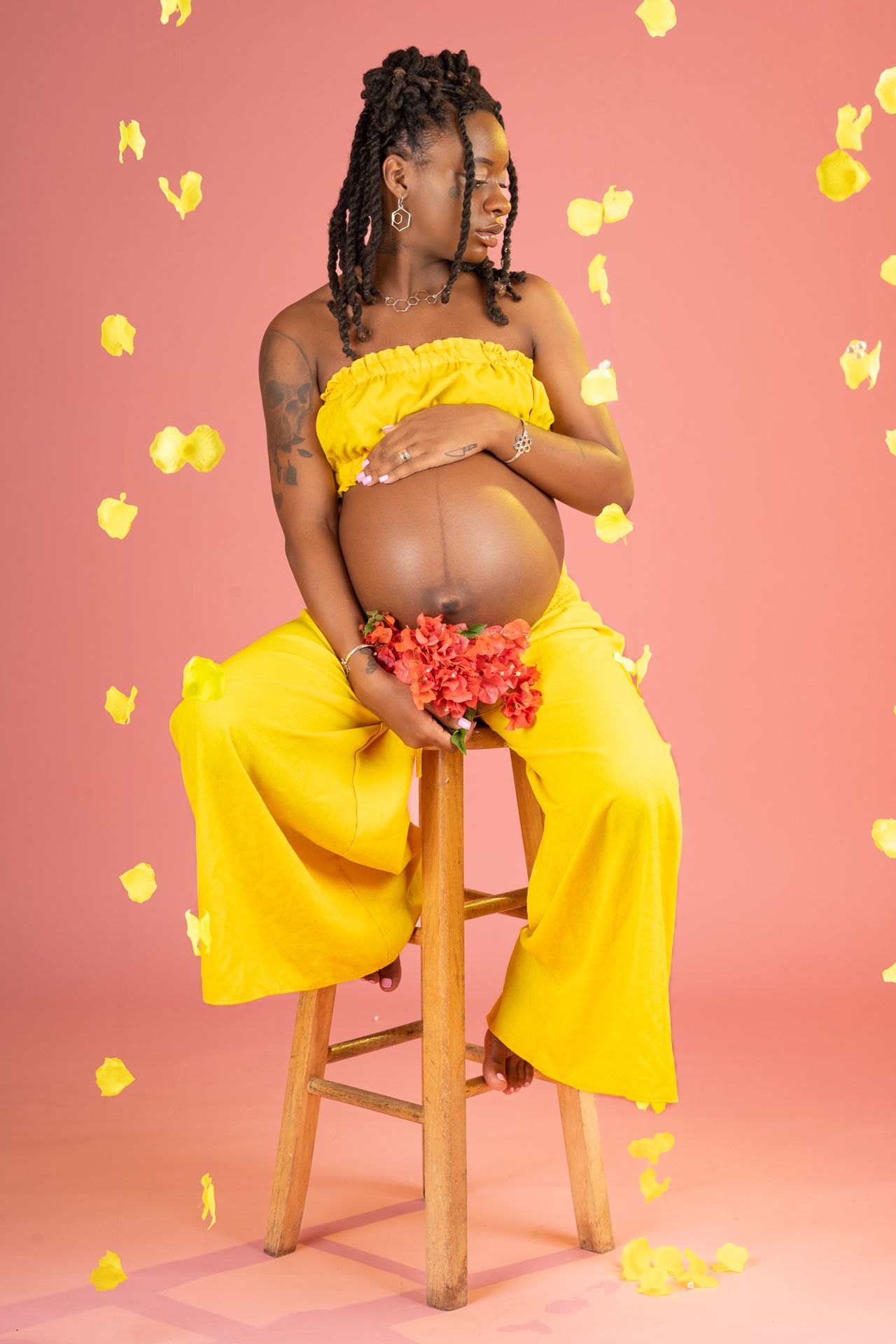 Maternity photo featuring a yellow dress and flowers against a coral background with floating petals.