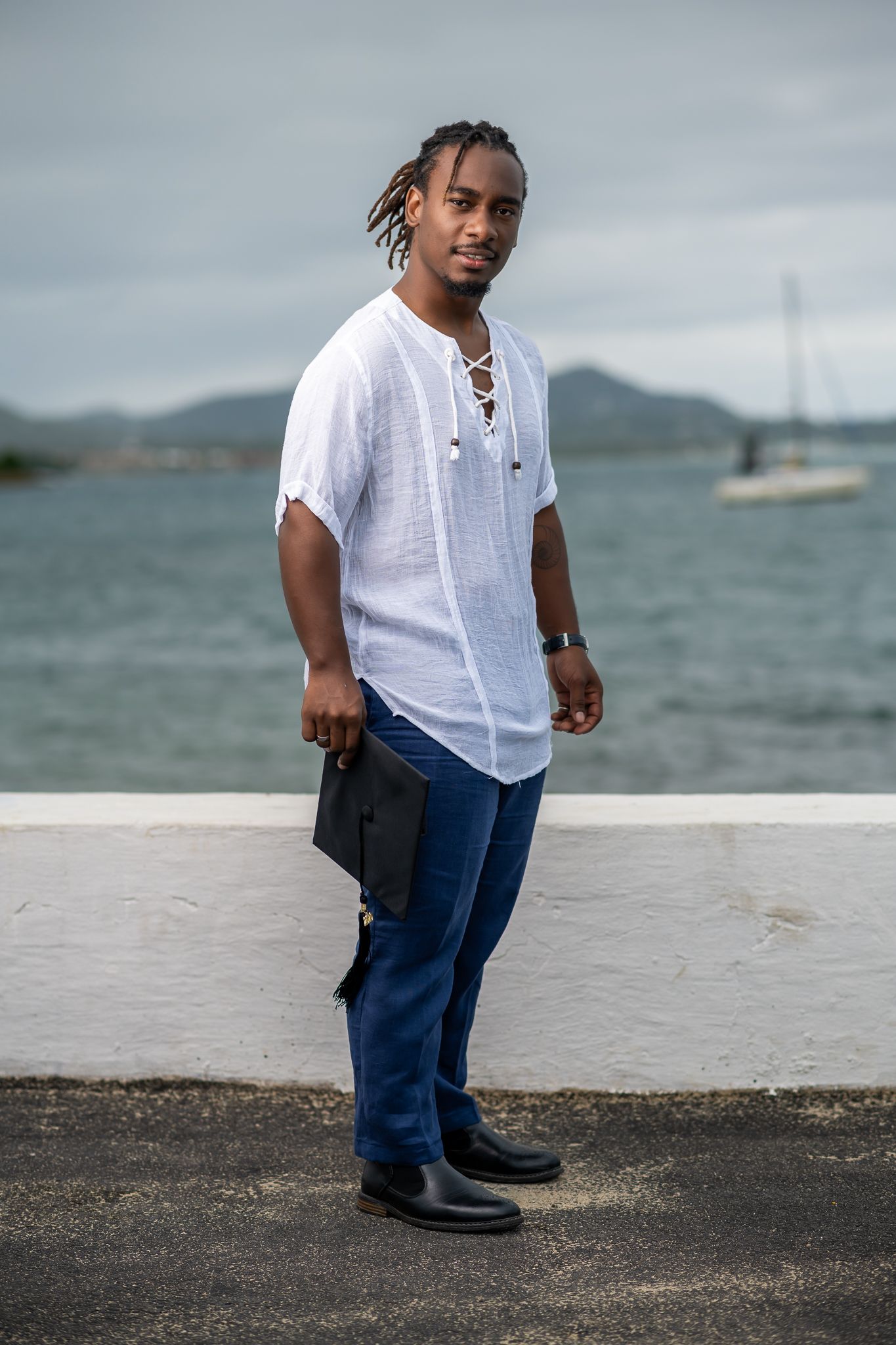 Casual coastal portrait in white linen shirt and jeans with boats and water in background.