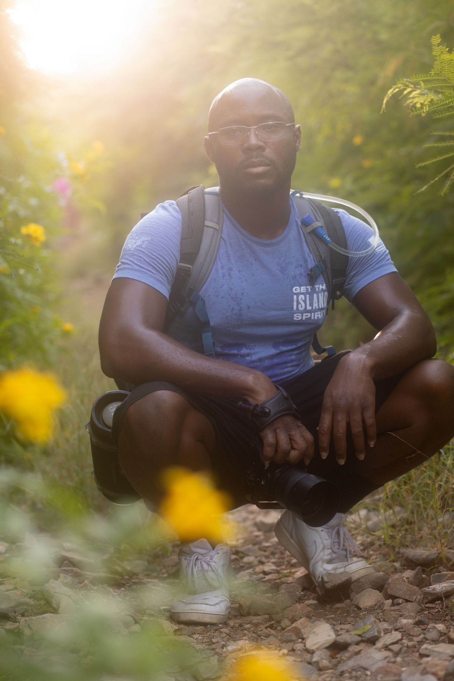 Person in blue t-shirt sitting casually on natural terrain with yellow flowers in foreground.