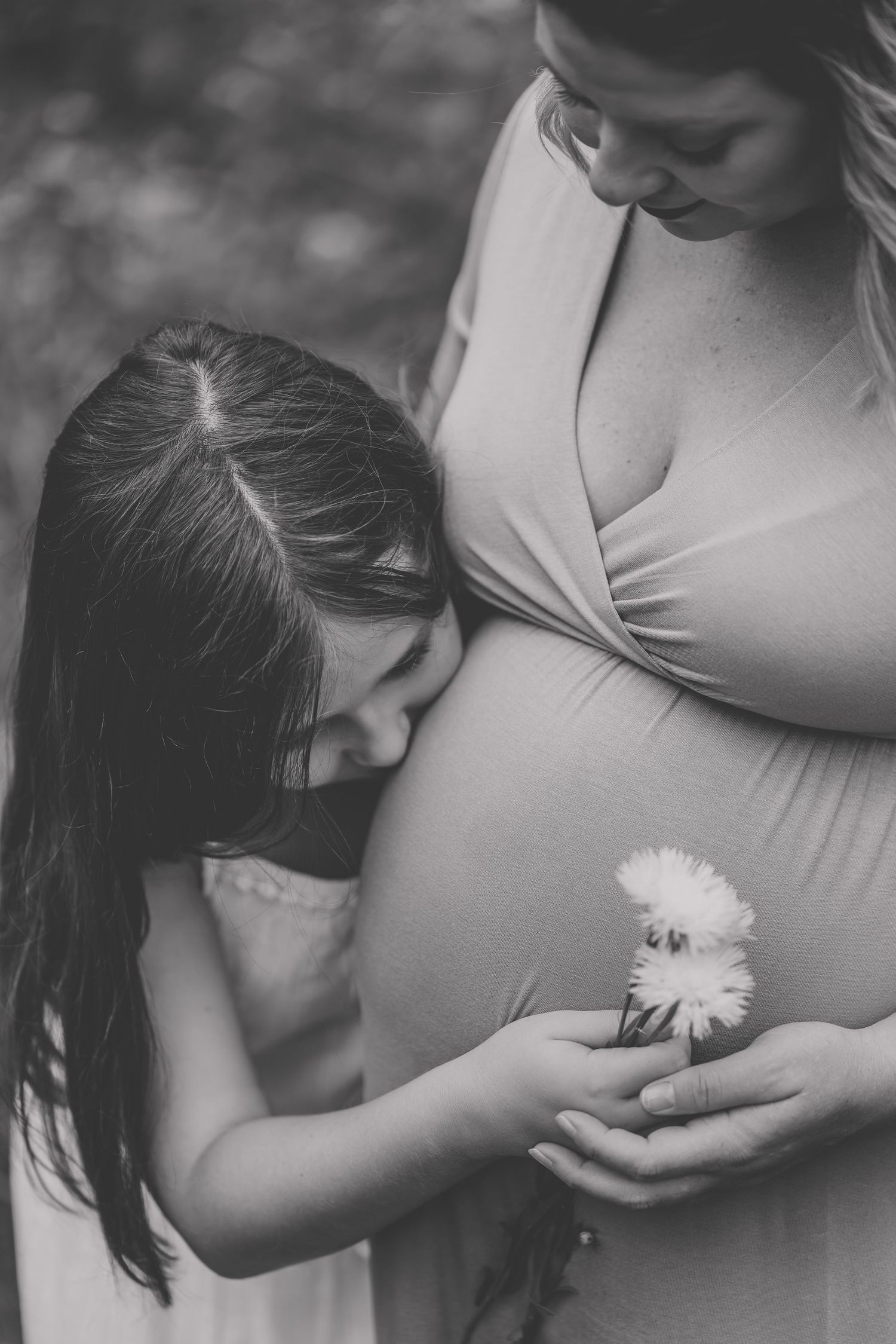 Black and white image of child holding flower near pregnant woman's belly.
