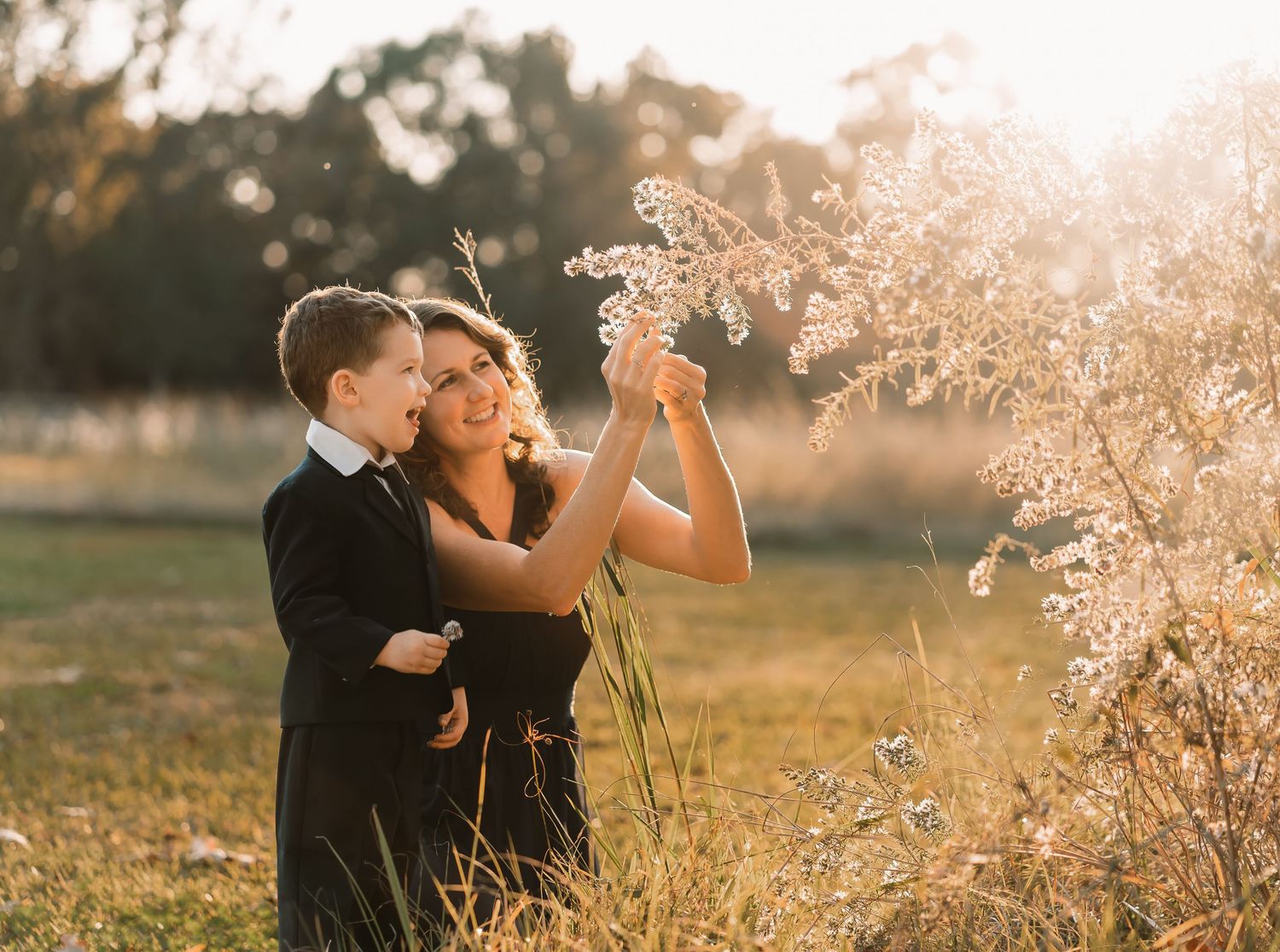 Two people playfully interact with tall grass during golden hour in a field.