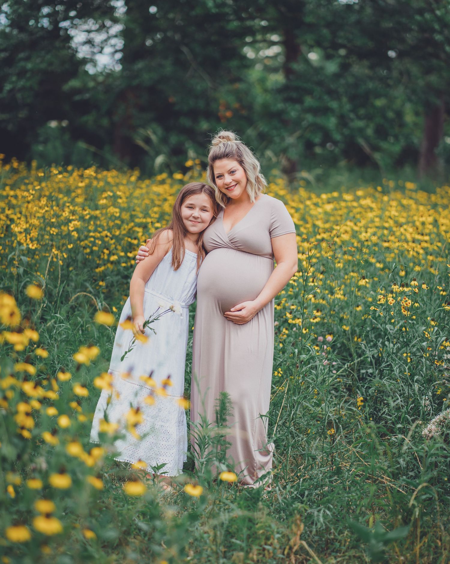 Mother and daughter pose together in field of yellow wildflowers on sunny day.