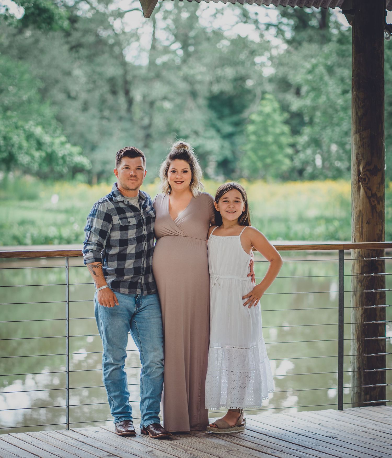 Family poses together on wooden deck with railing and natural scenery in background.