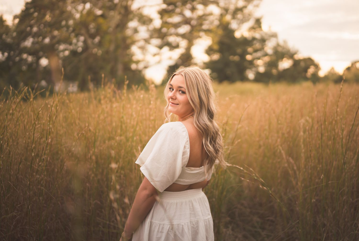 A person in a white dress walks through a golden field at sunset, creating a dreamy summer atmosphere.