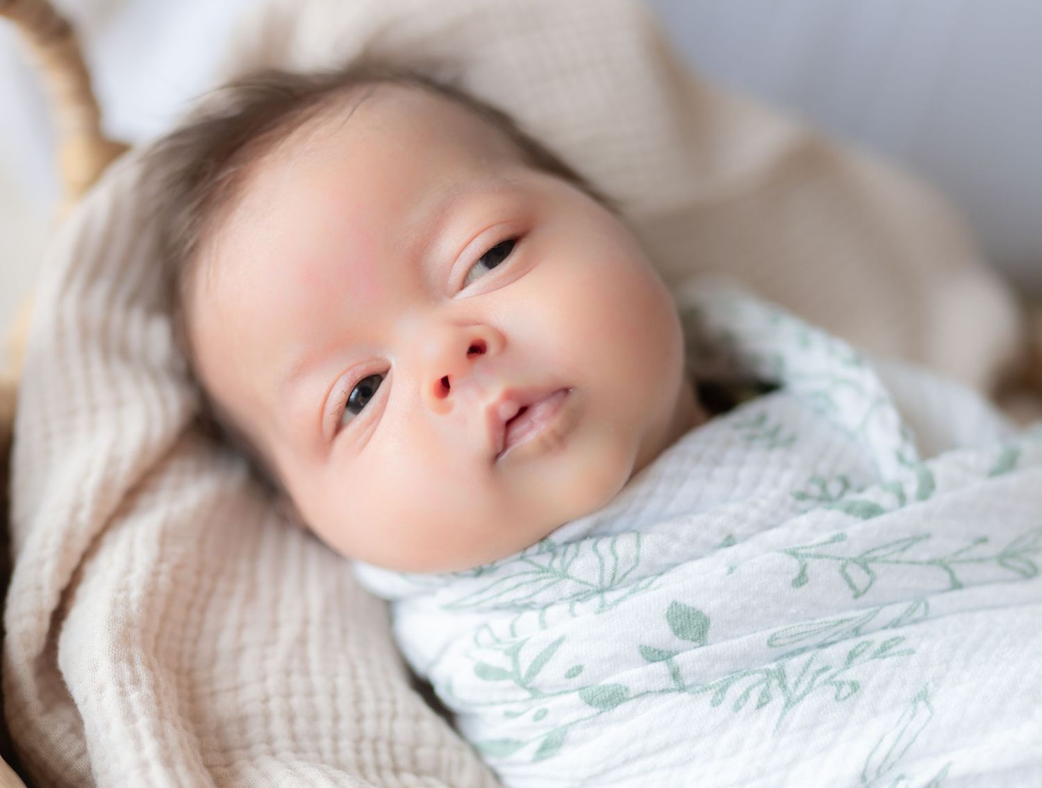 A sleeping baby lies peacefully on soft beige bedding with a gentle expression on their face.