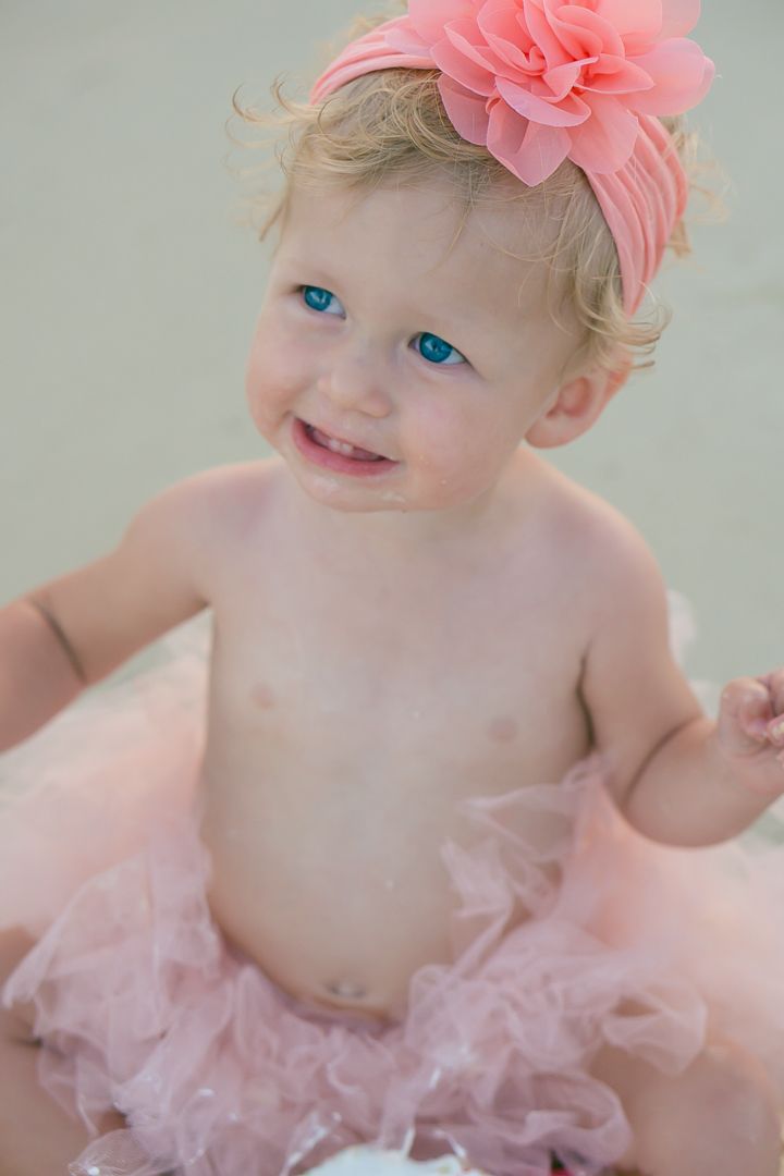 Toddler wearing pink flower headband and tutu smiling during beach photoshoot.