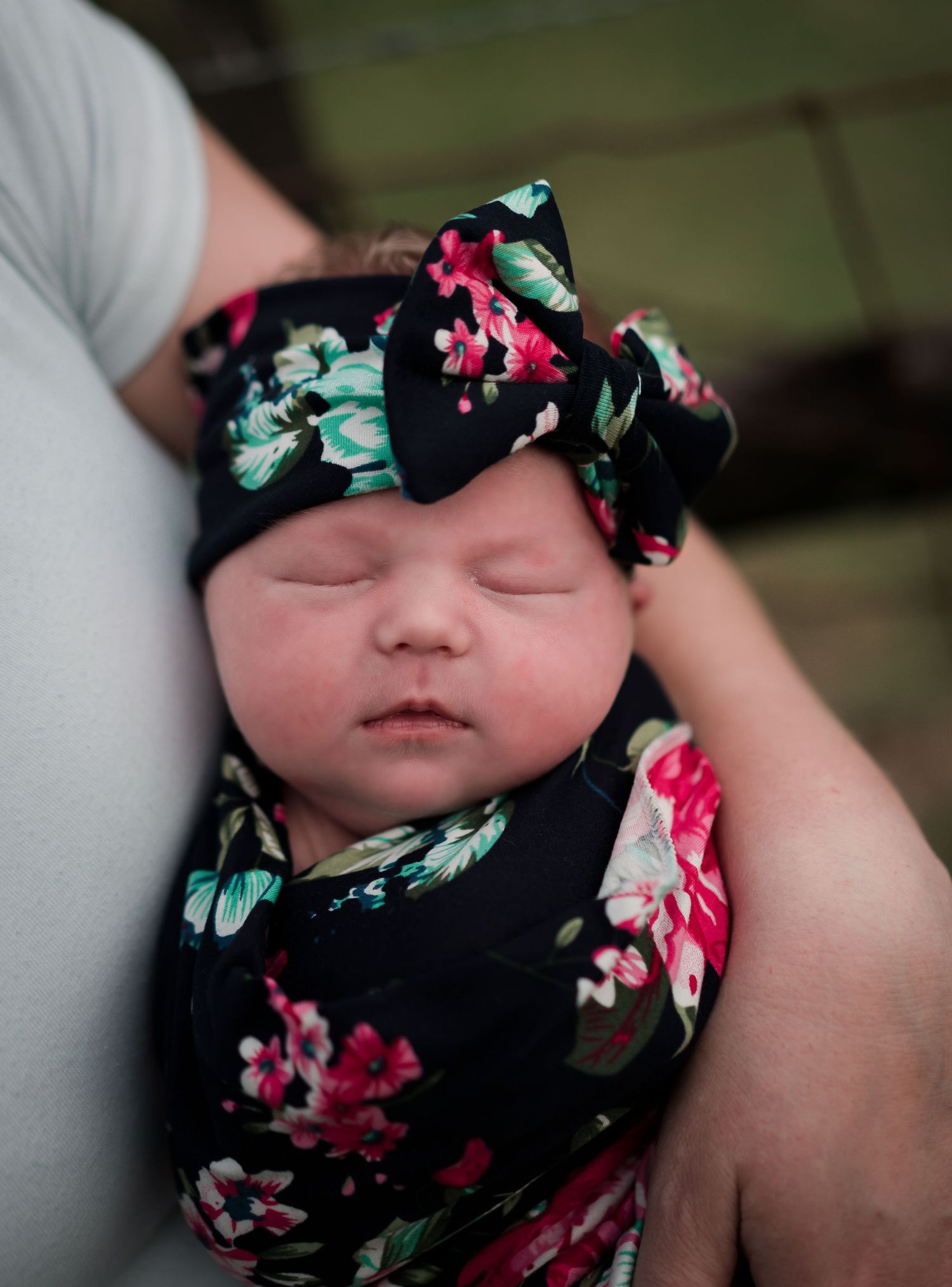 Sleeping infant wearing floral headband and matching outfit resting against white fabric.