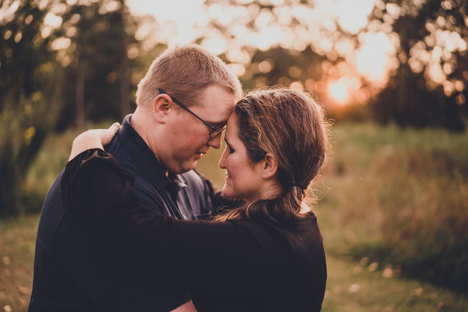 Intimate romantic portrait of couple embracing at sunset in field.