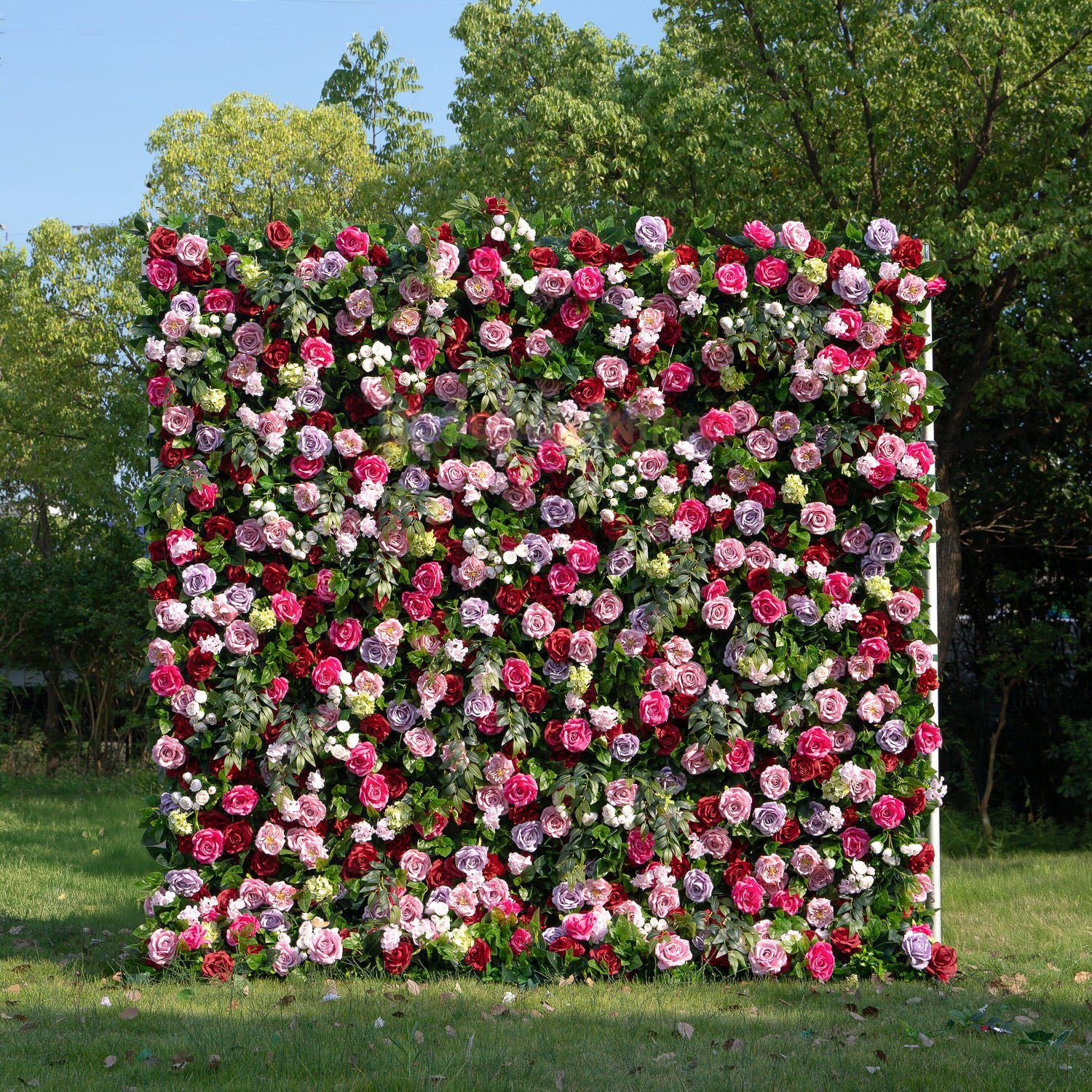 A lush flower wall installation featuring pink and white roses against a green garden background.