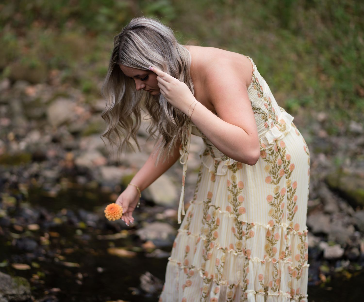 A series of photos showing someone in a floral dress bending down to touch water in a natural outdoor setting.