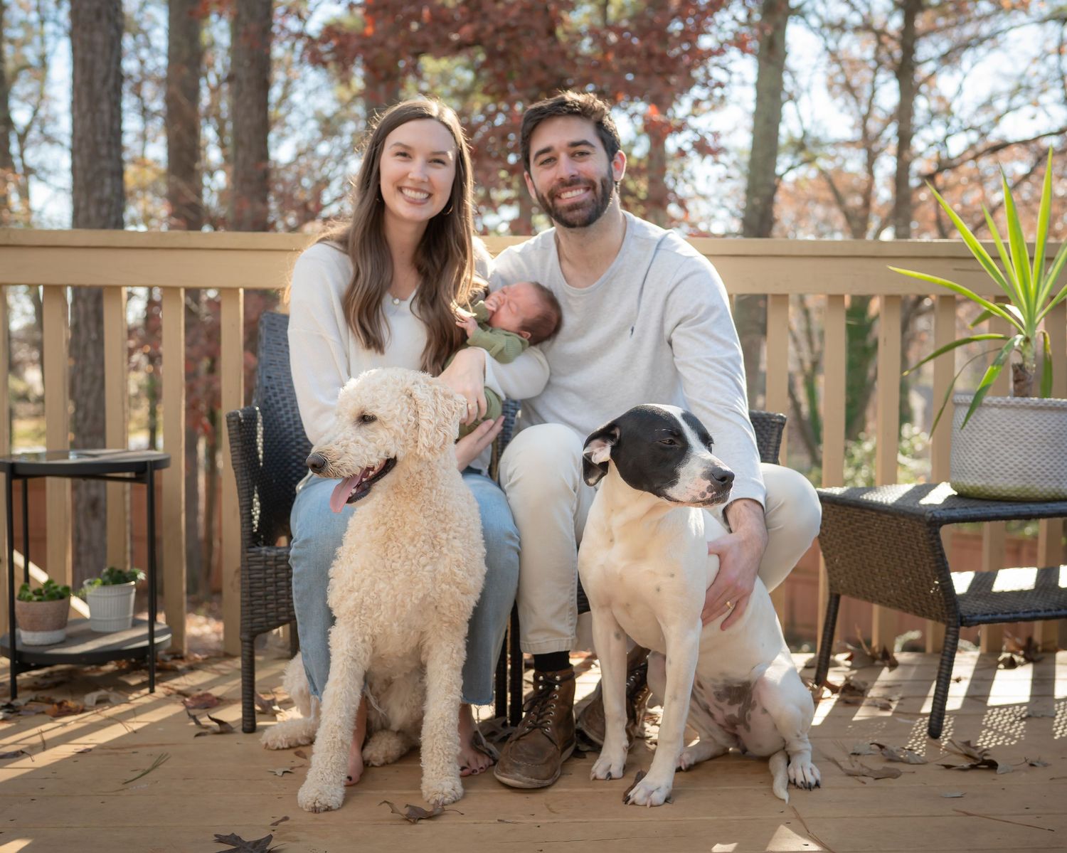 A couple sits on a deck with their two dogs, a white fluffy dog and a black and white dog.