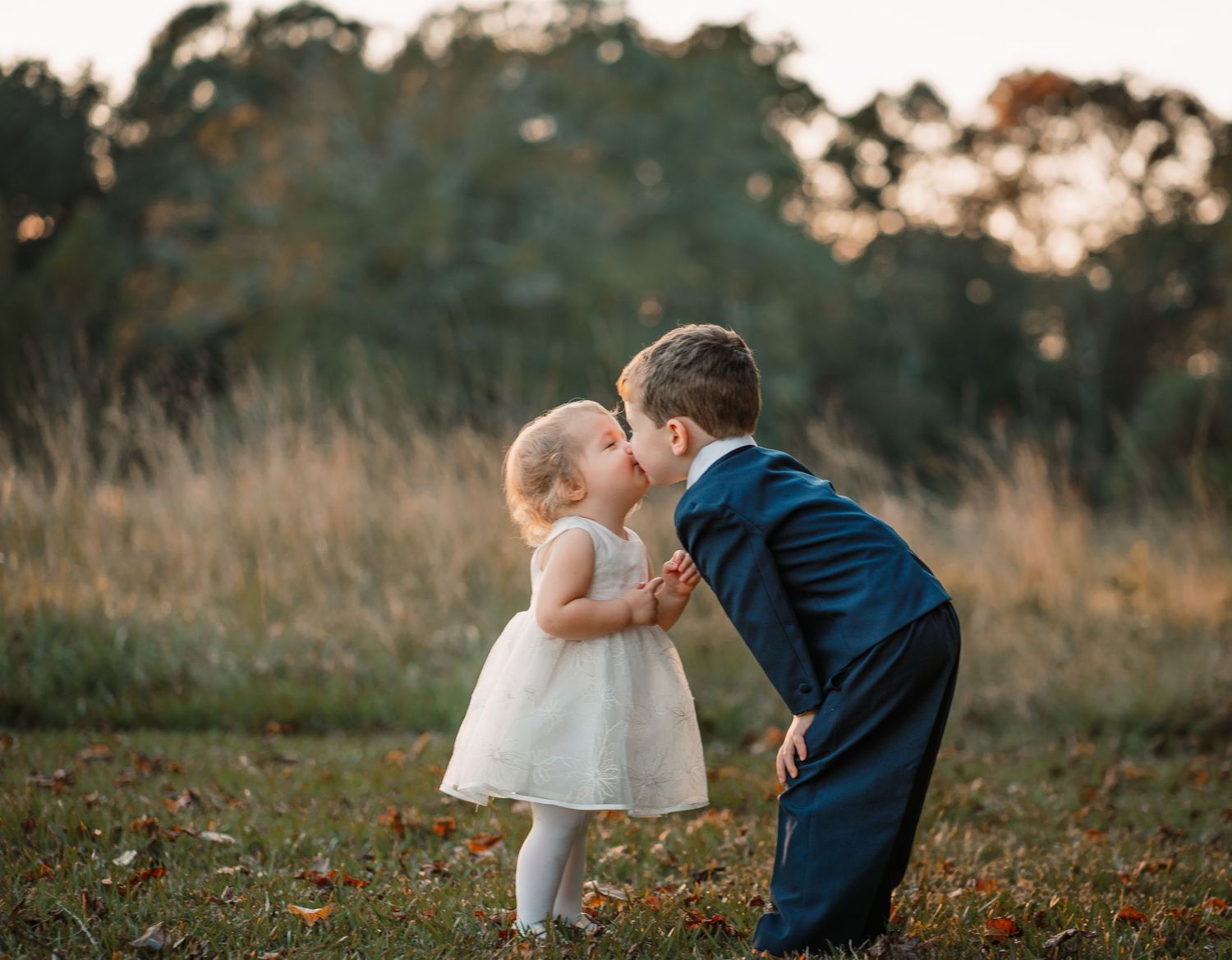 Sweet childhood moment between children in formal wear outdoors at sunset.