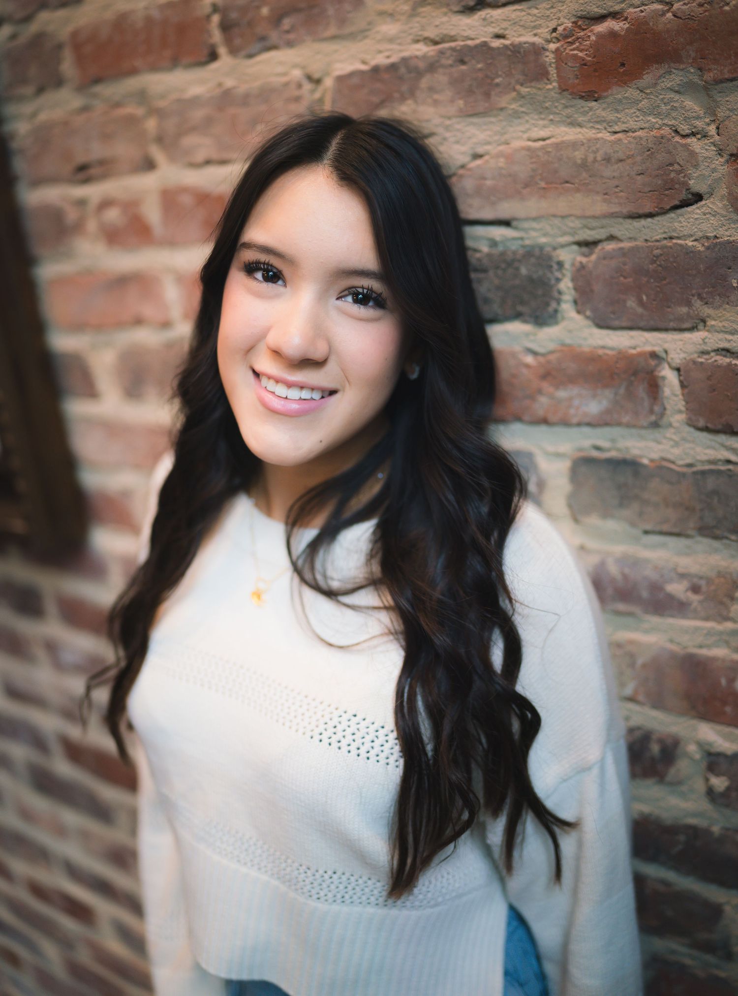 A series of four portrait photos against a rustic brick wall background showing long dark hair and a white sweater.