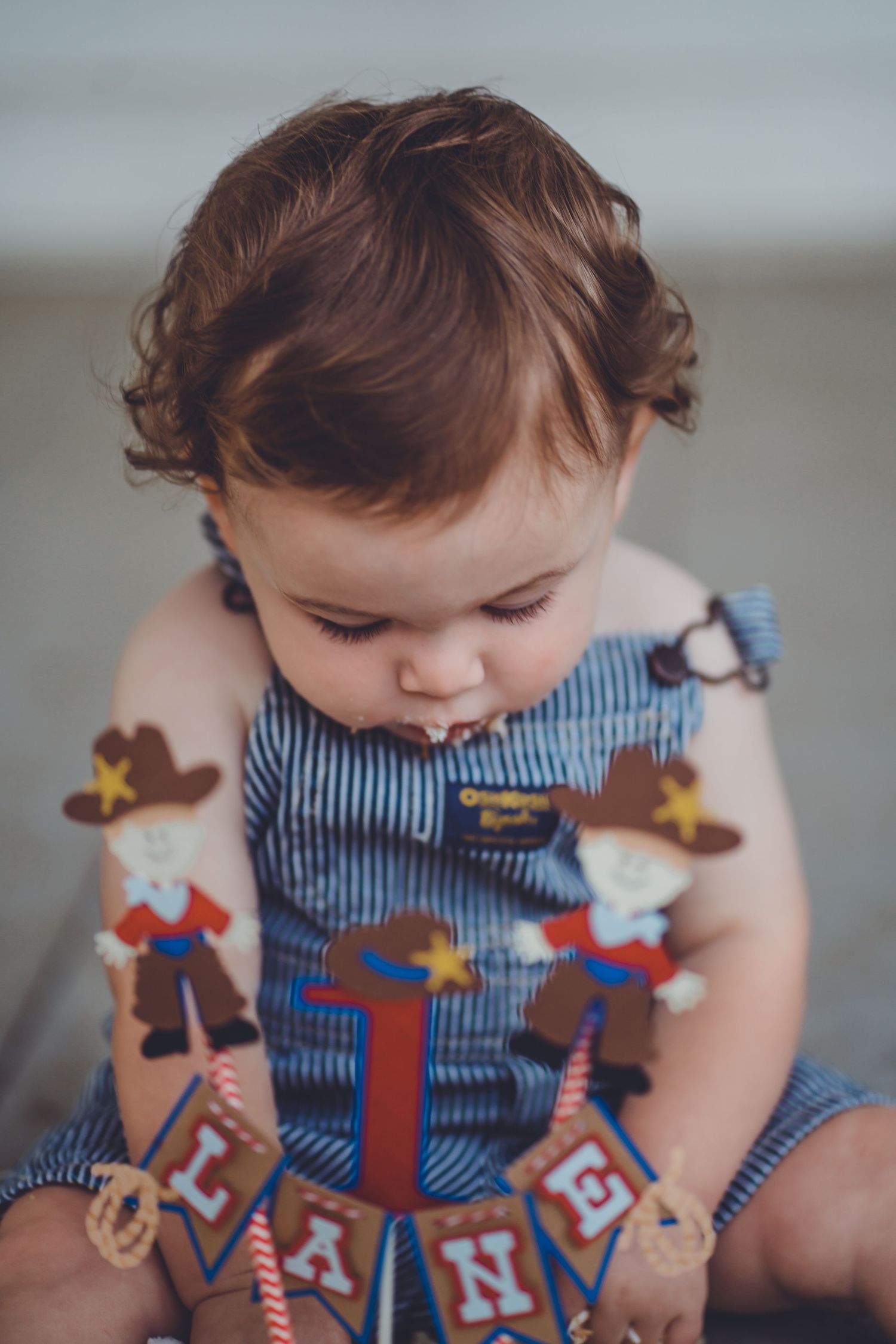 Small child in striped overalls looks down at western-themed party decorations.