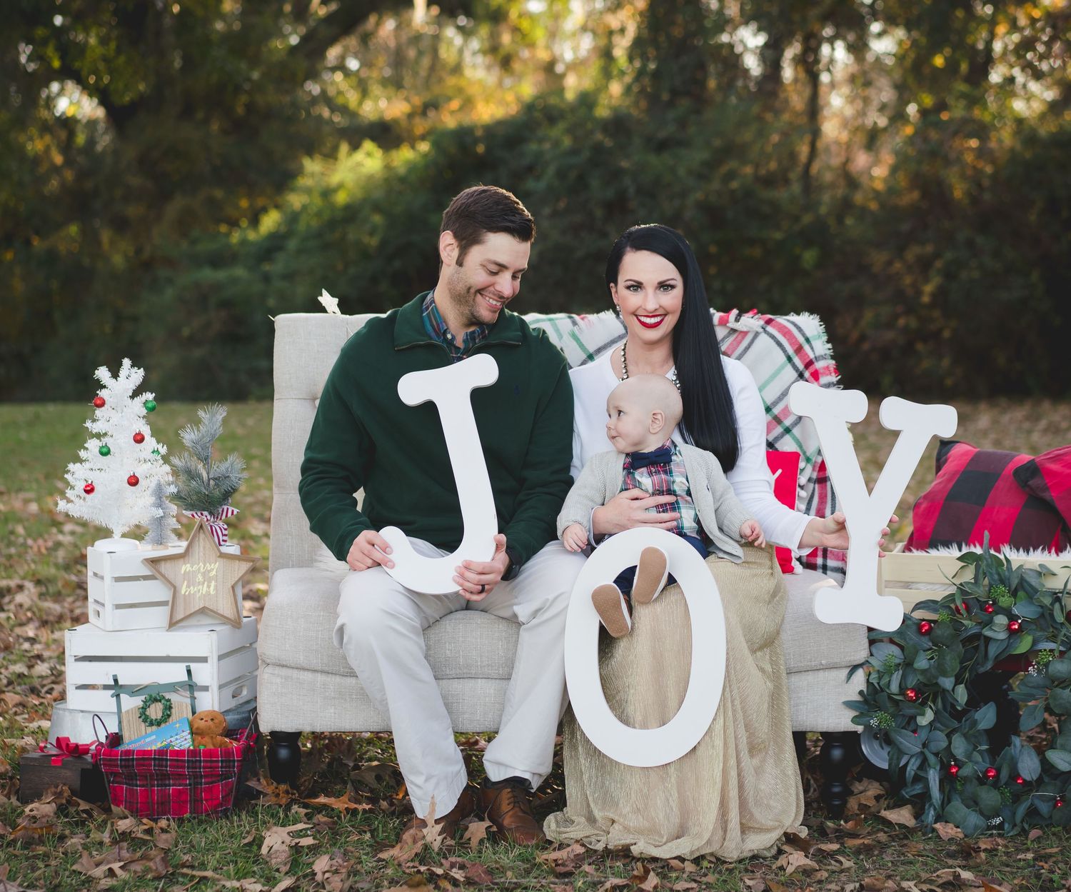 Holiday themed outdoor photo setup with couch, JOY letters, wrapped presents and winter decorations.