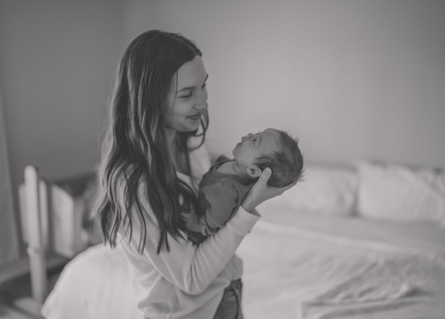 A tender black and white photograph captures a parent lovingly holding their newborn baby in a bedroom setting.
