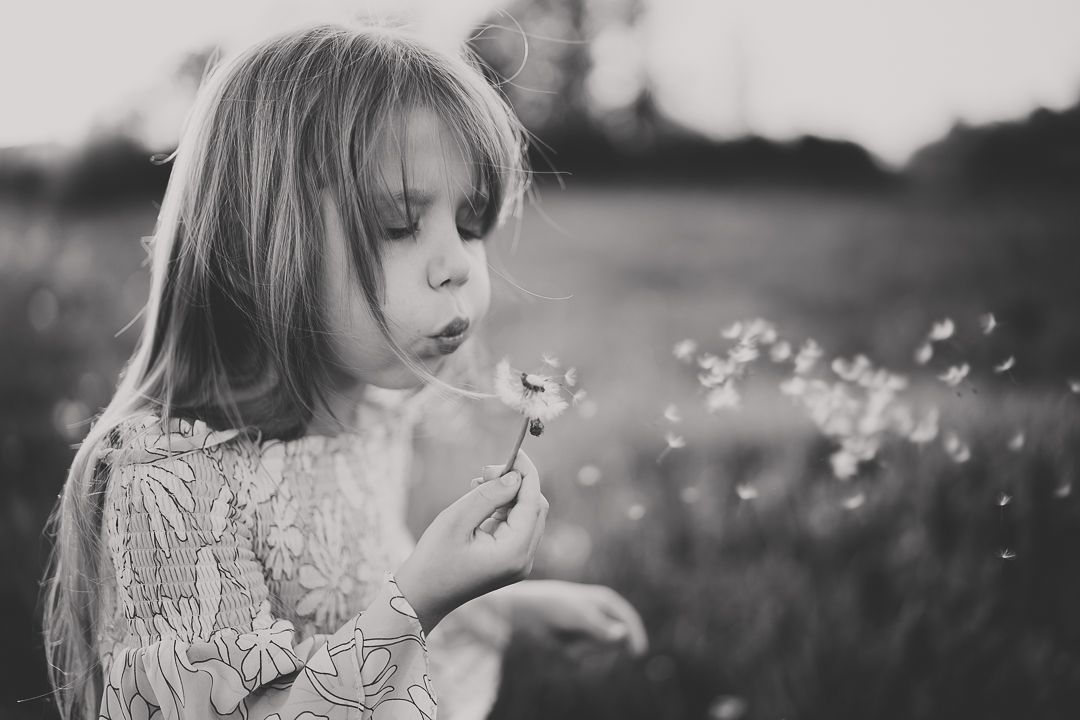 Child blowing dandelion seeds in a dreamy black and white field scene with soft bokeh background.