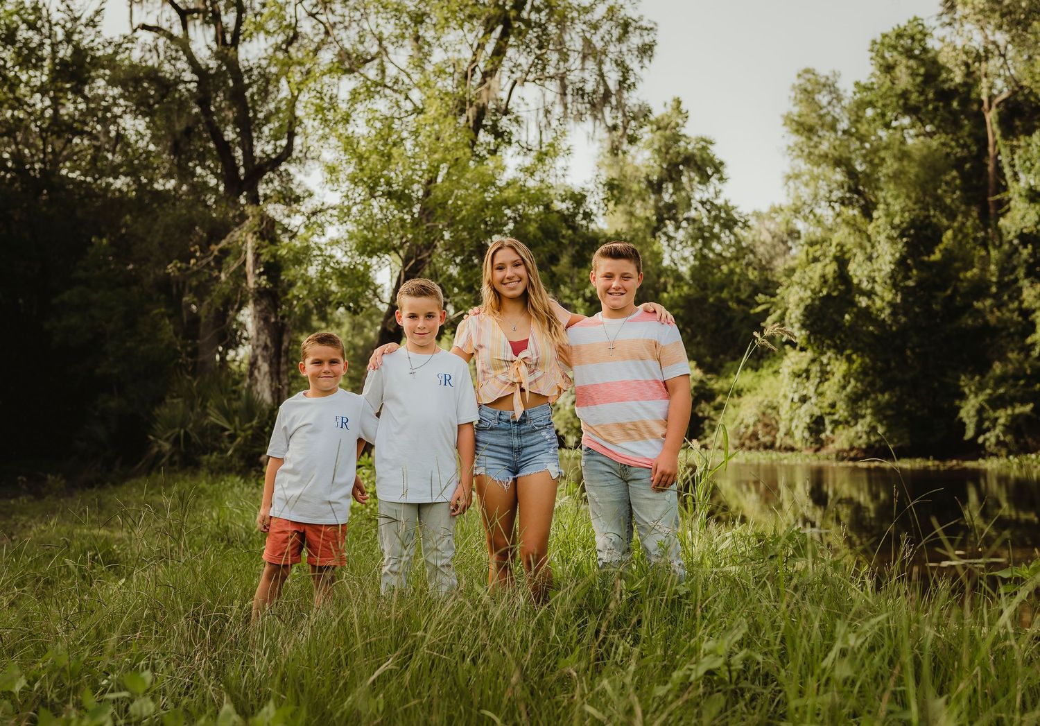 A casual family portrait of people standing together by a pond in summer evening light.