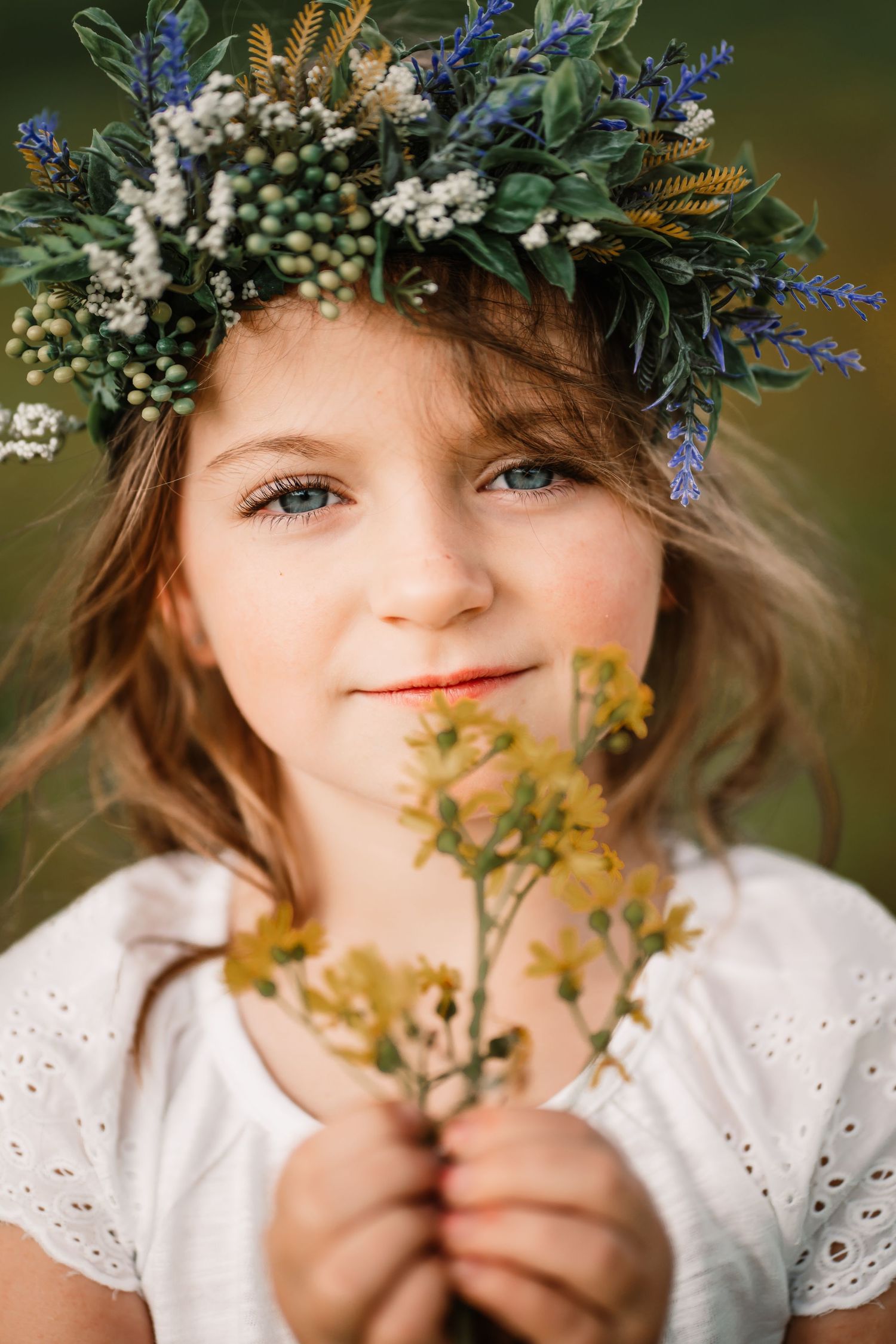 Portrait featuring a beautiful floral crown made of blue flowers and berries with a white eyelet dress.