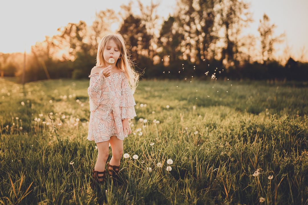 Golden hour portrait of child wearing dress and boots in wildflower field.