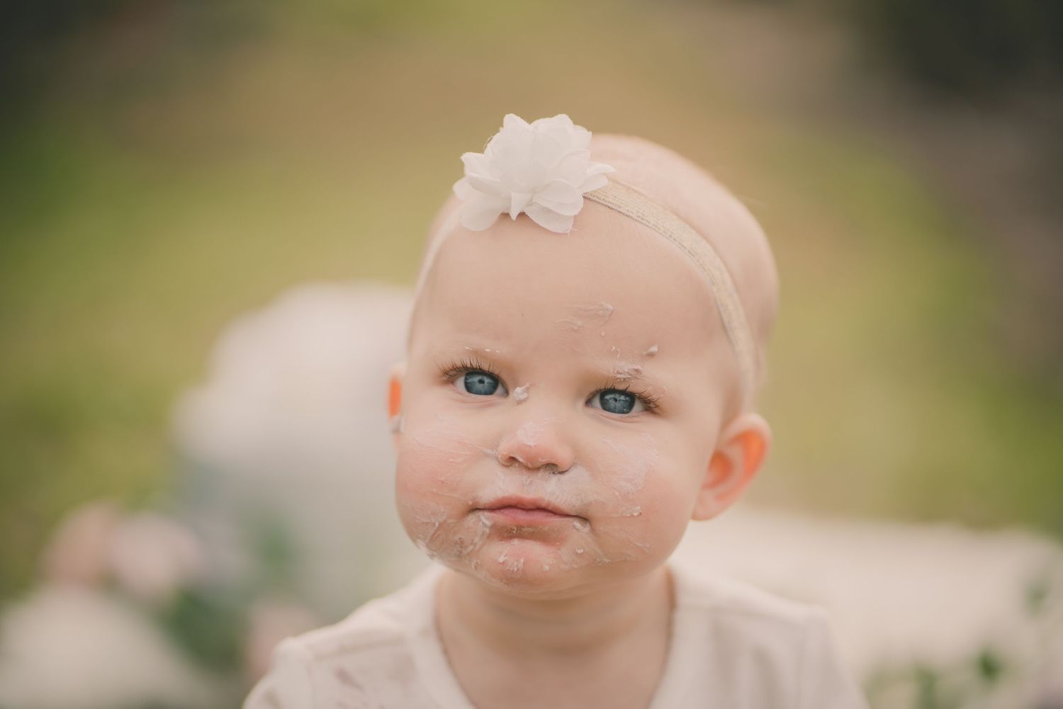 Close up portrait of a baby wearing a delicate white headband against a soft blurred background.