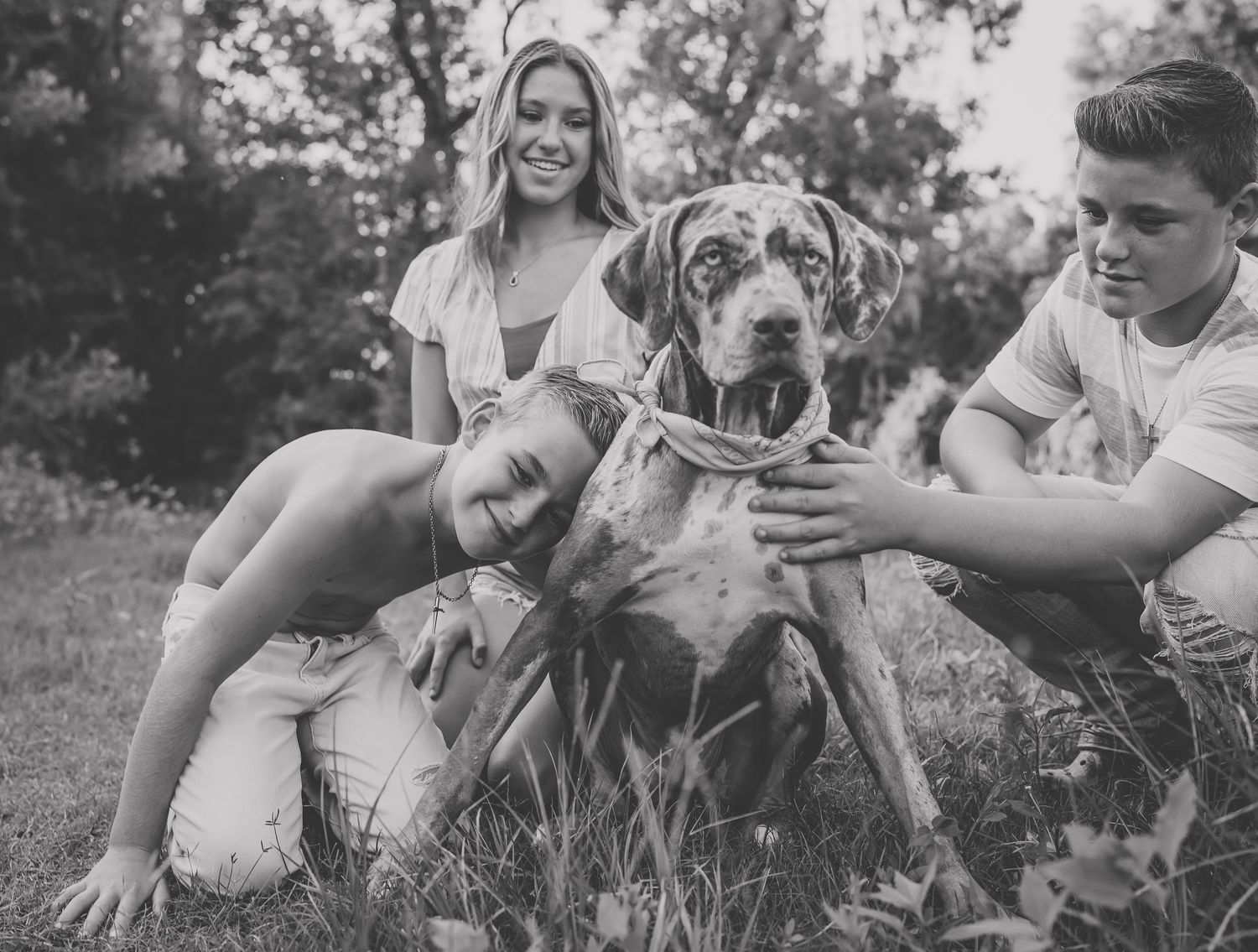 A happy family and their Great Dane pet dog pose together on grassy field in black and white.