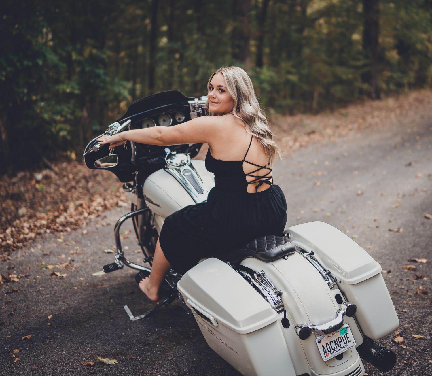 A woman poses on a white motorcycle on a forest path during autumn.
