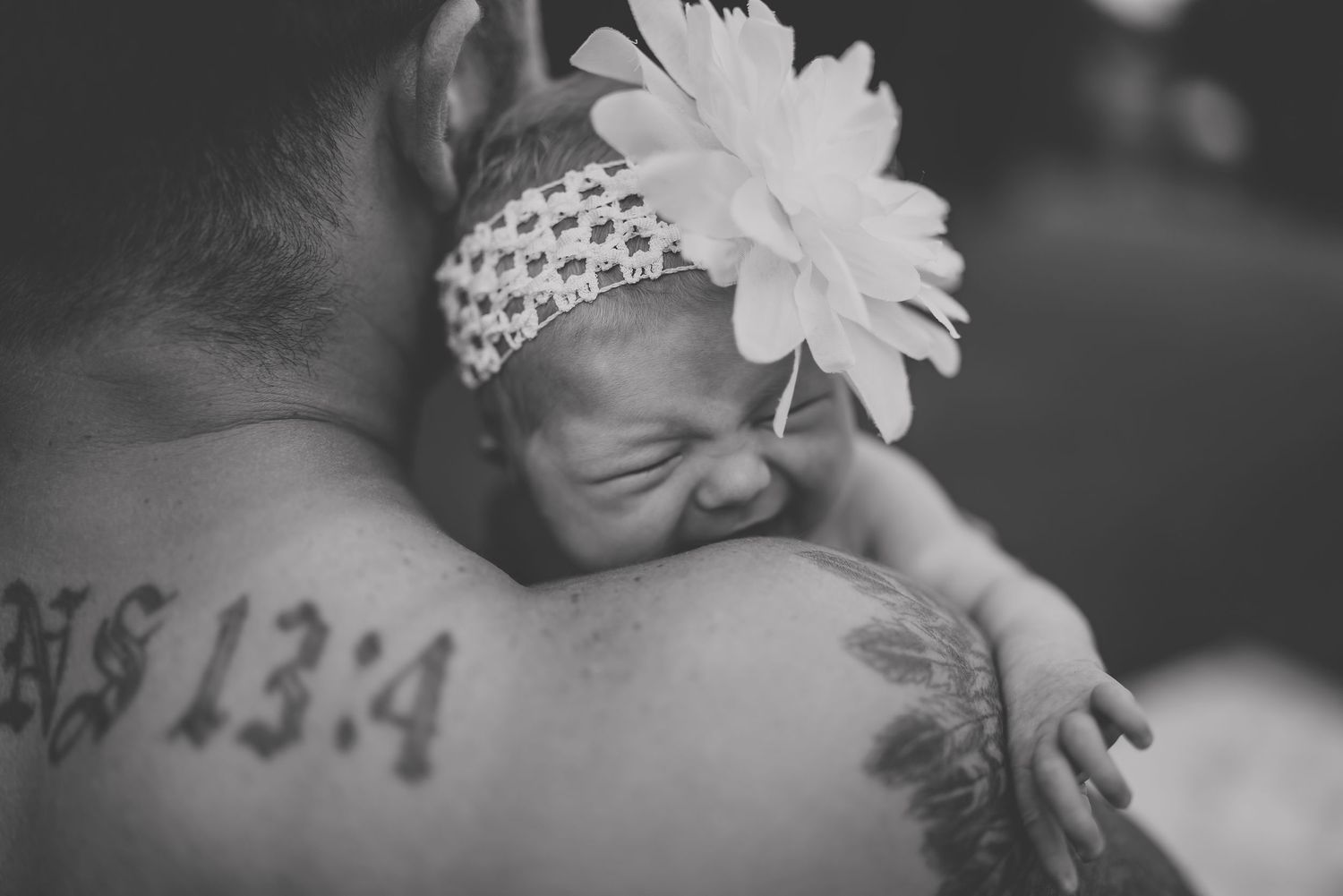 Black and white portrait of a crying infant wearing a white headband with flower.