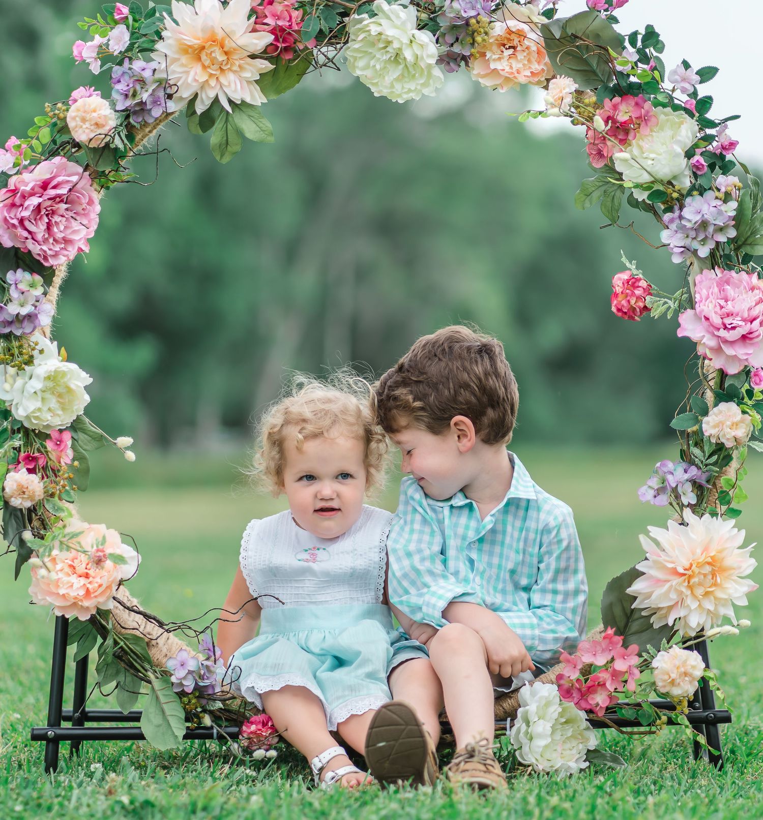 Children sitting under beautiful floral arch in garden setting during spring photo session.