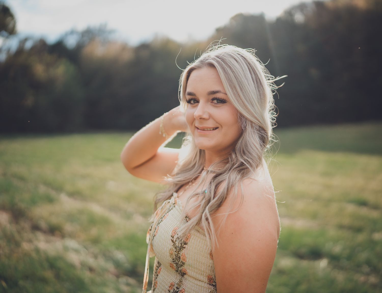 Woman with blonde hair poses outdoors in a field at sunset wearing a floral dress.