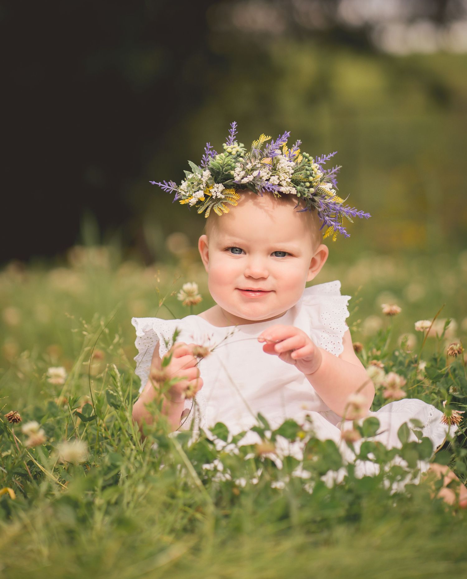 Sweet summer portrait of a tiny subject wearing a floral crown and white dress in a meadow.