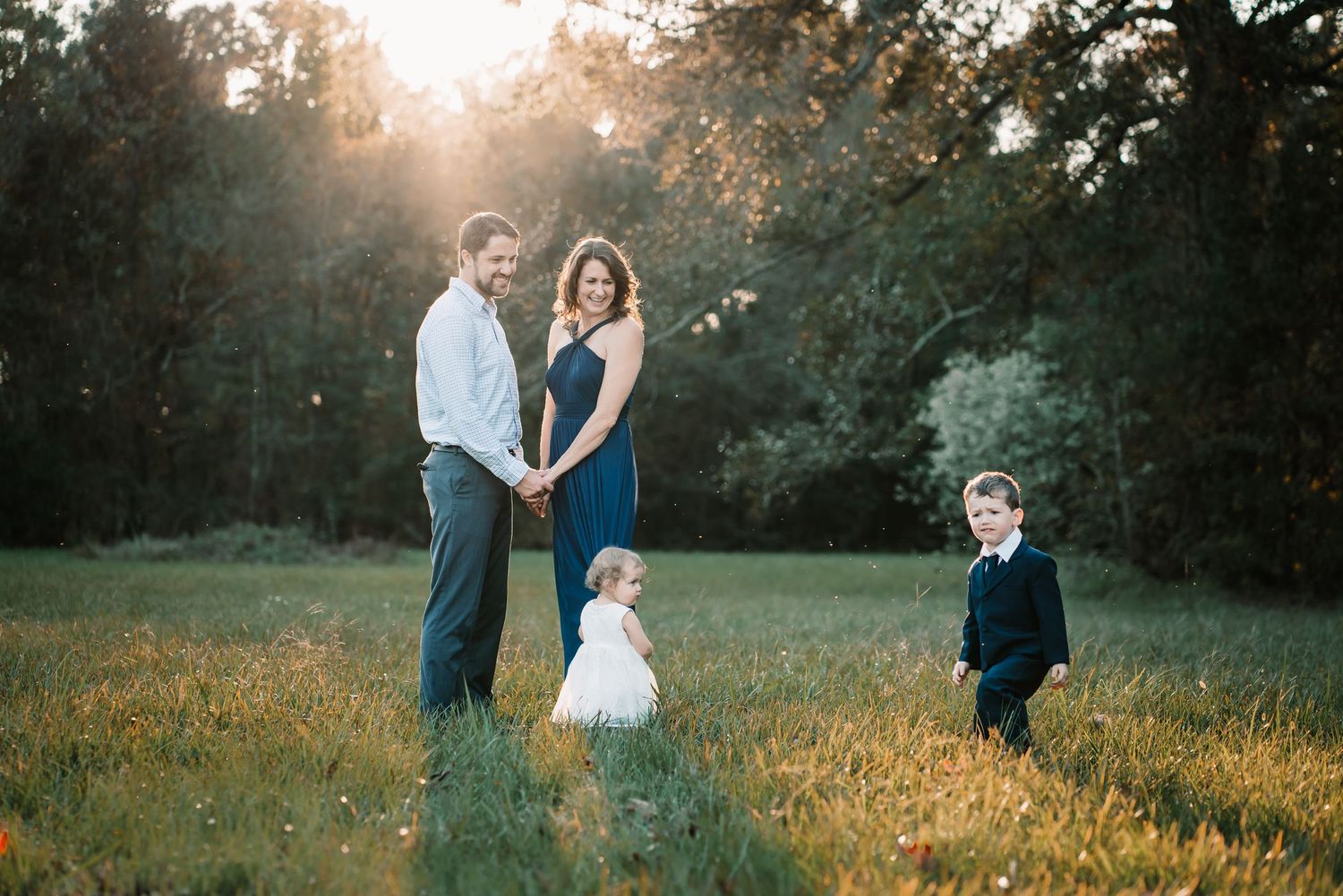 A family stands together in a grassy field during golden hour.