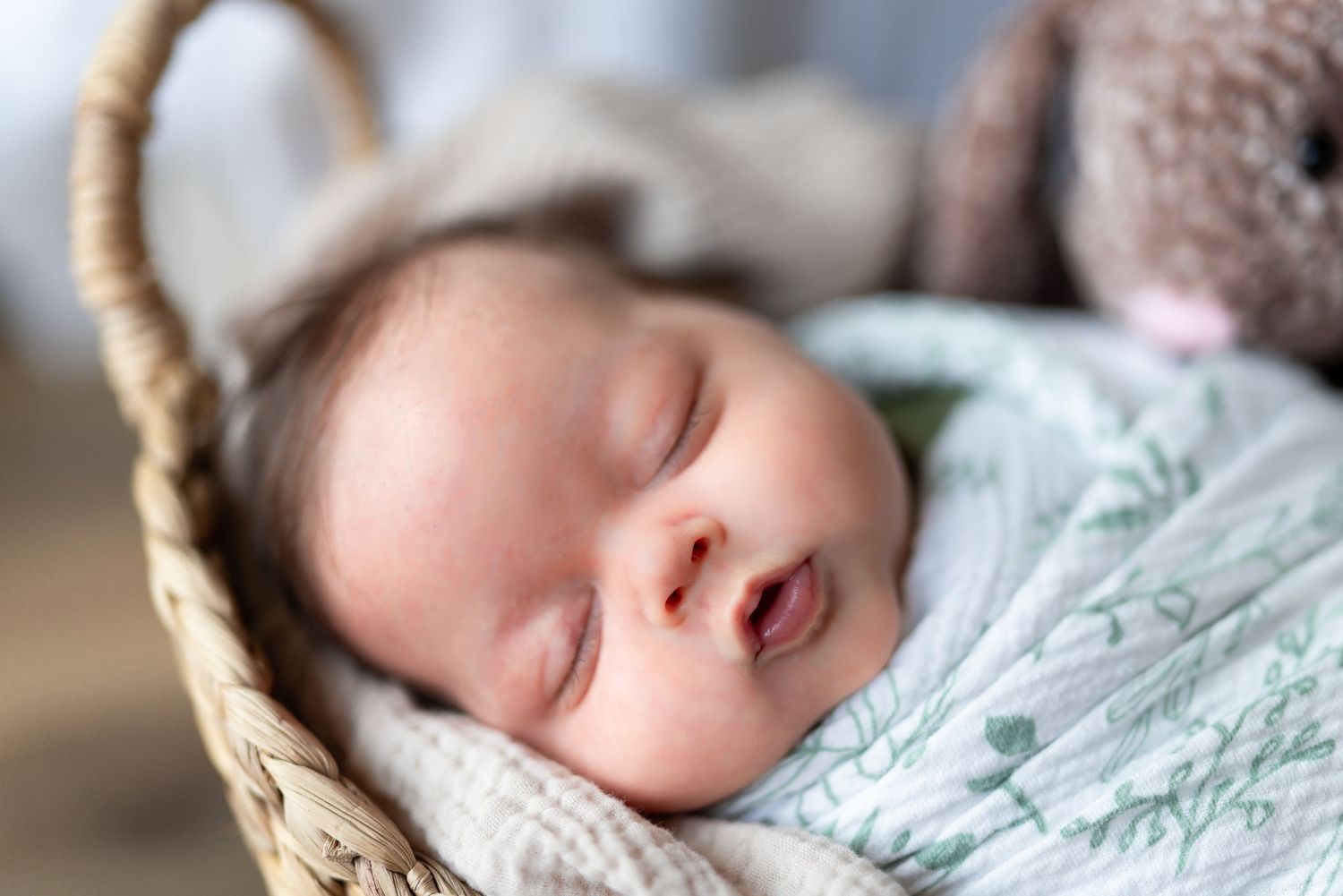 A sleeping newborn baby wrapped in soft mint green swaddle blanket rests peacefully in a cozy basket.