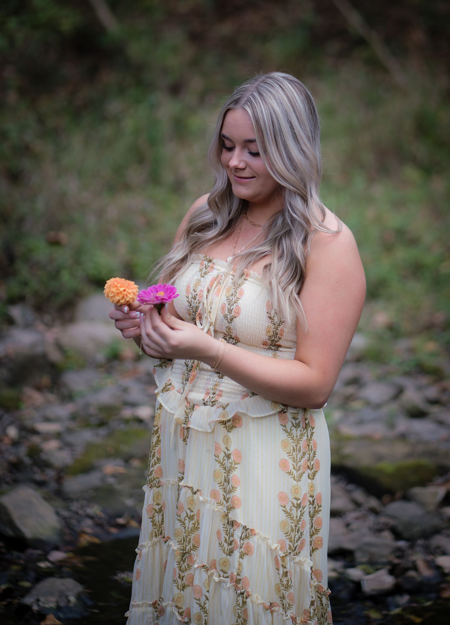 A floral dress photoshoot by a creek with natural elements and soft lighting creating a romantic atmosphere.
