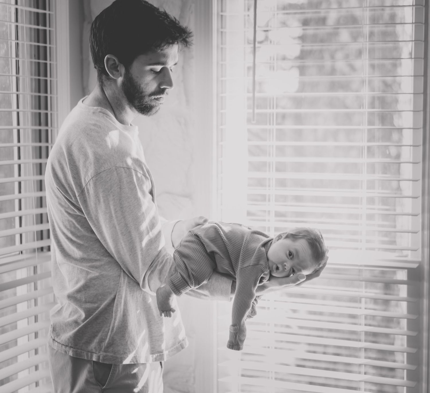 Black and white photos of a parent and baby bonding near a window with venetian blinds.