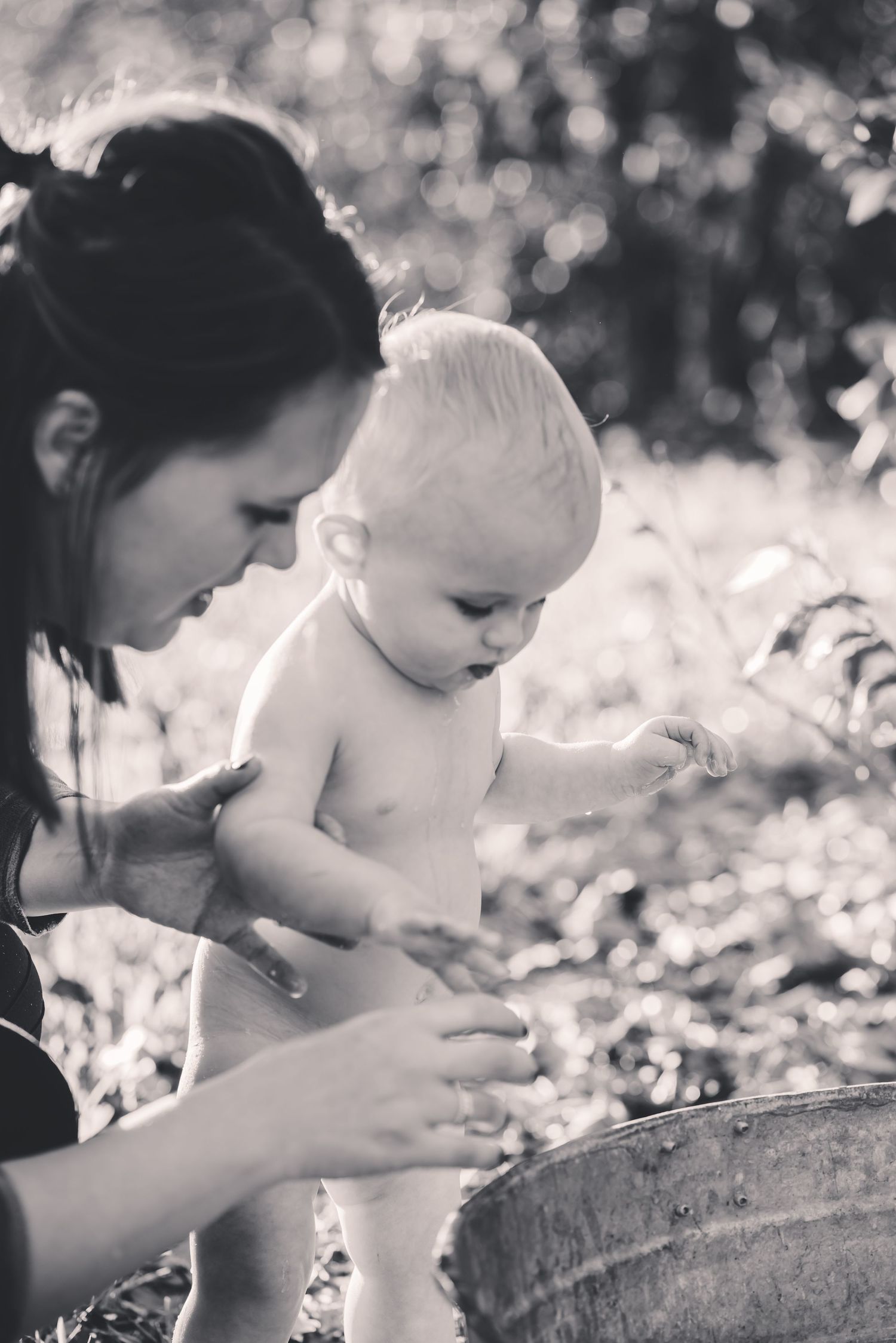 Black and white photo of baby being bathed in vintage washtub outdoors.