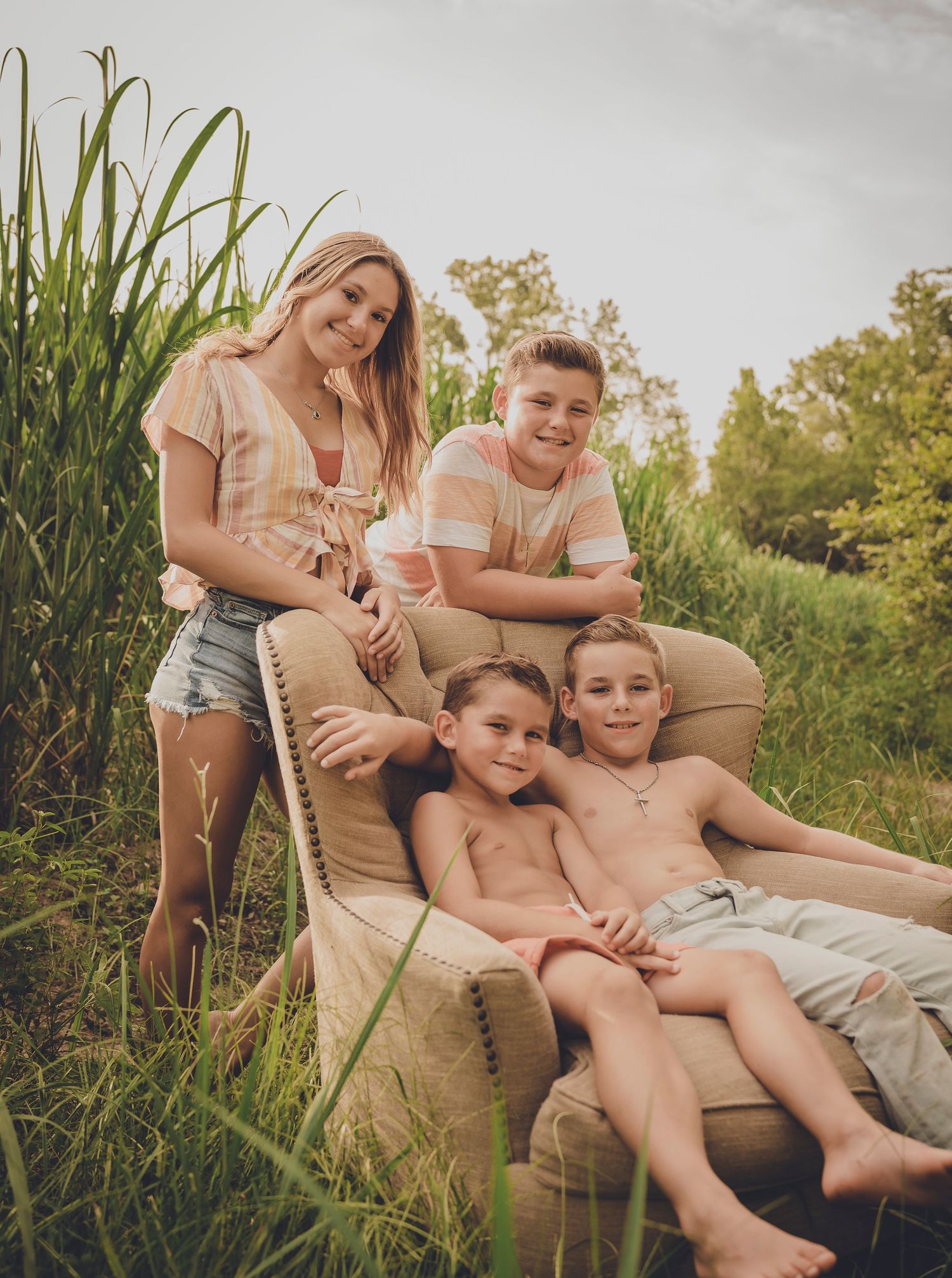 Family relaxing on beige couch positioned outdoors among tall grass.