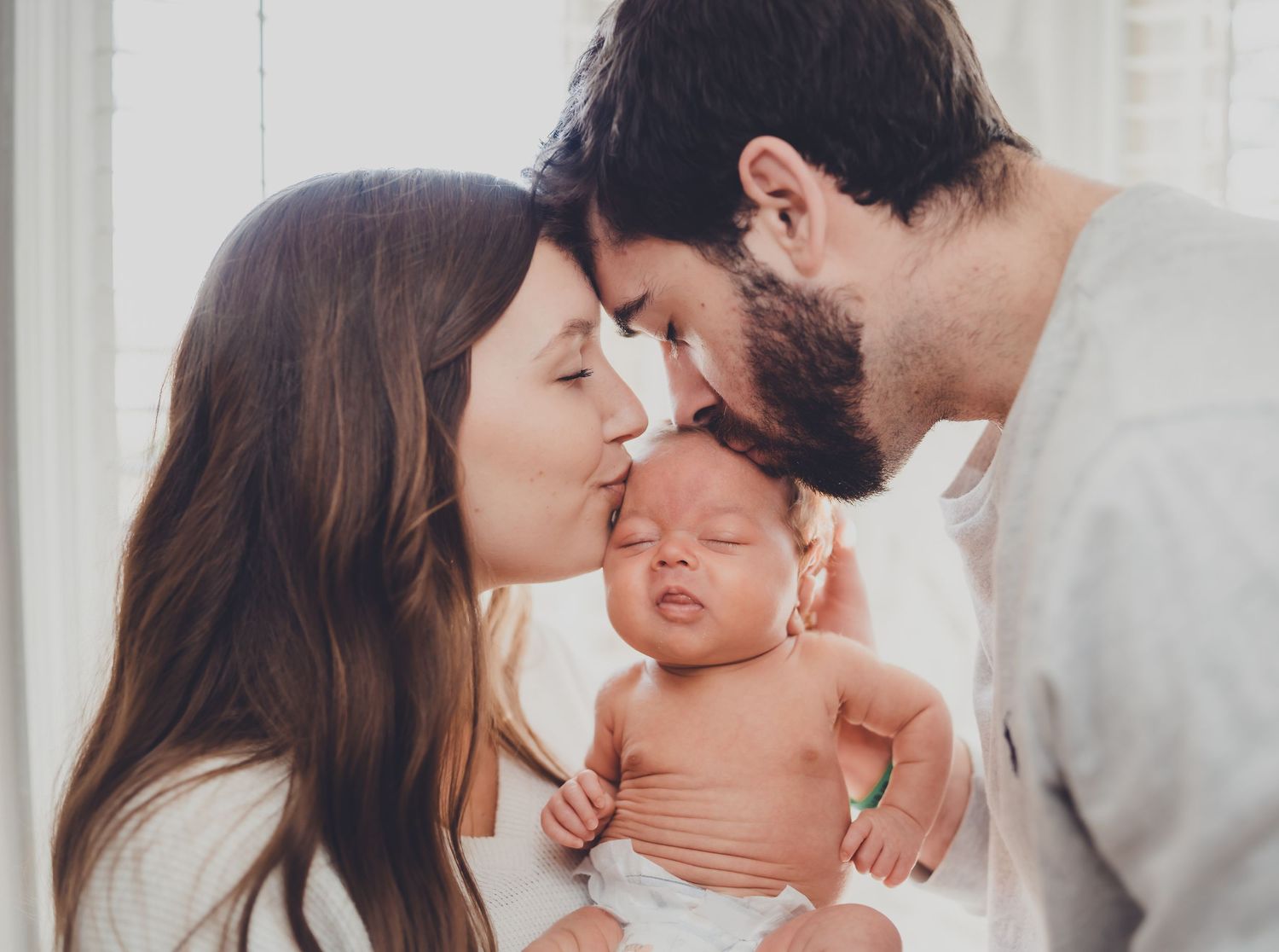 A tender moment between parents and their sleeping newborn baby as they share gentle kisses.