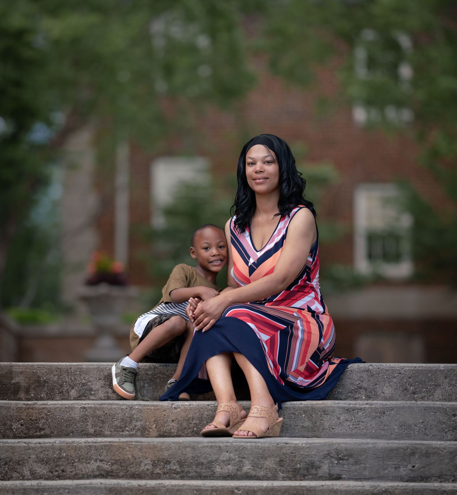 A parent and child sit together on outdoor stone steps wearing colorful clothing on a sunny day.