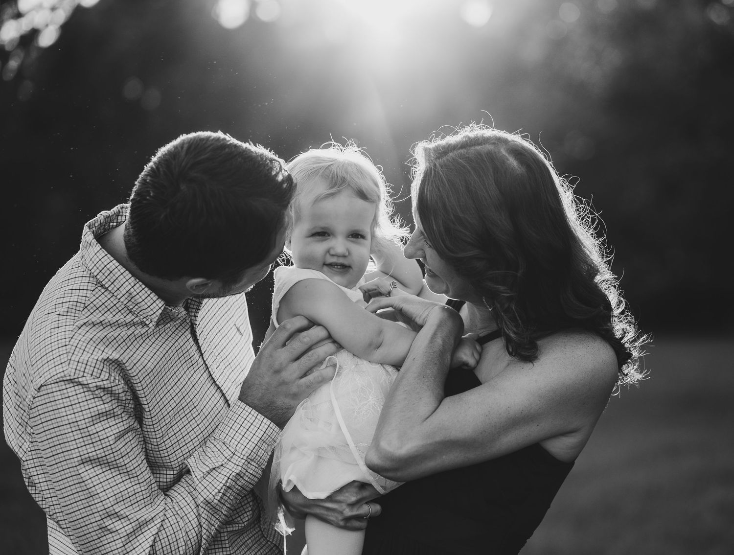 An intimate black and white portrait of a family sharing a tender moment outdoors.