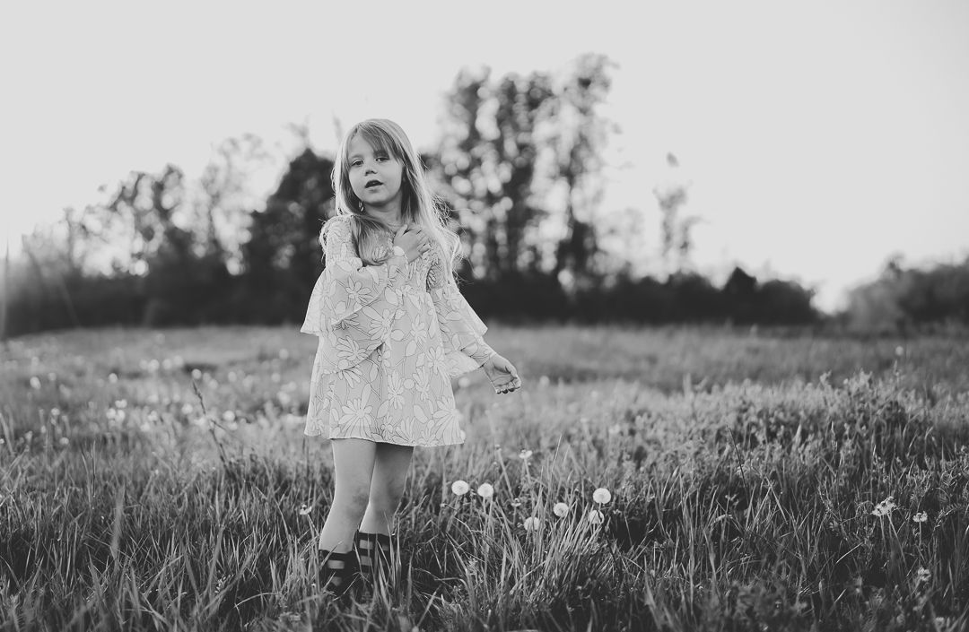 Black and white portrait of child in flowy dress standing in field.
