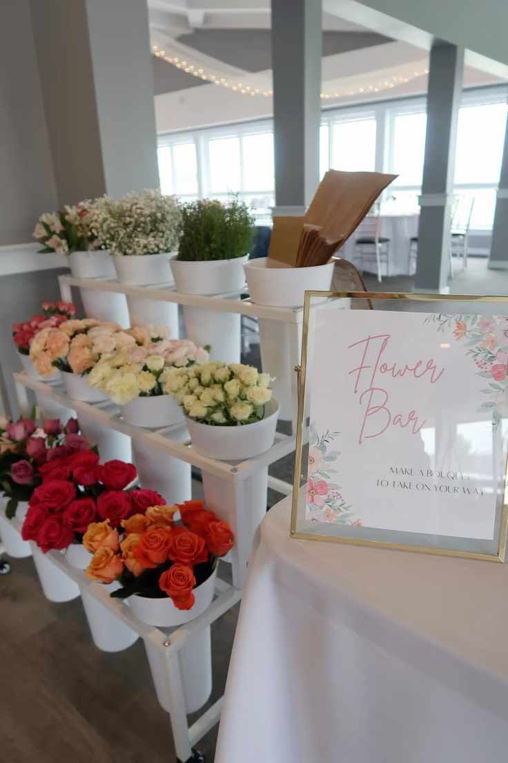 White floral display stands with pink and red roses arranged at a wedding venue with elegant name cards and signage.