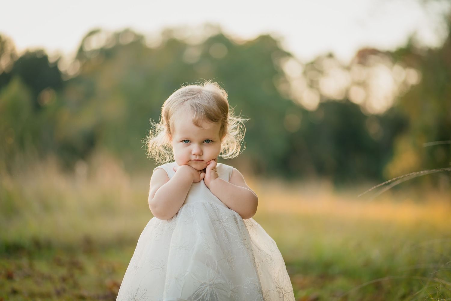 A small child in a white dress stands in a sunlit field.