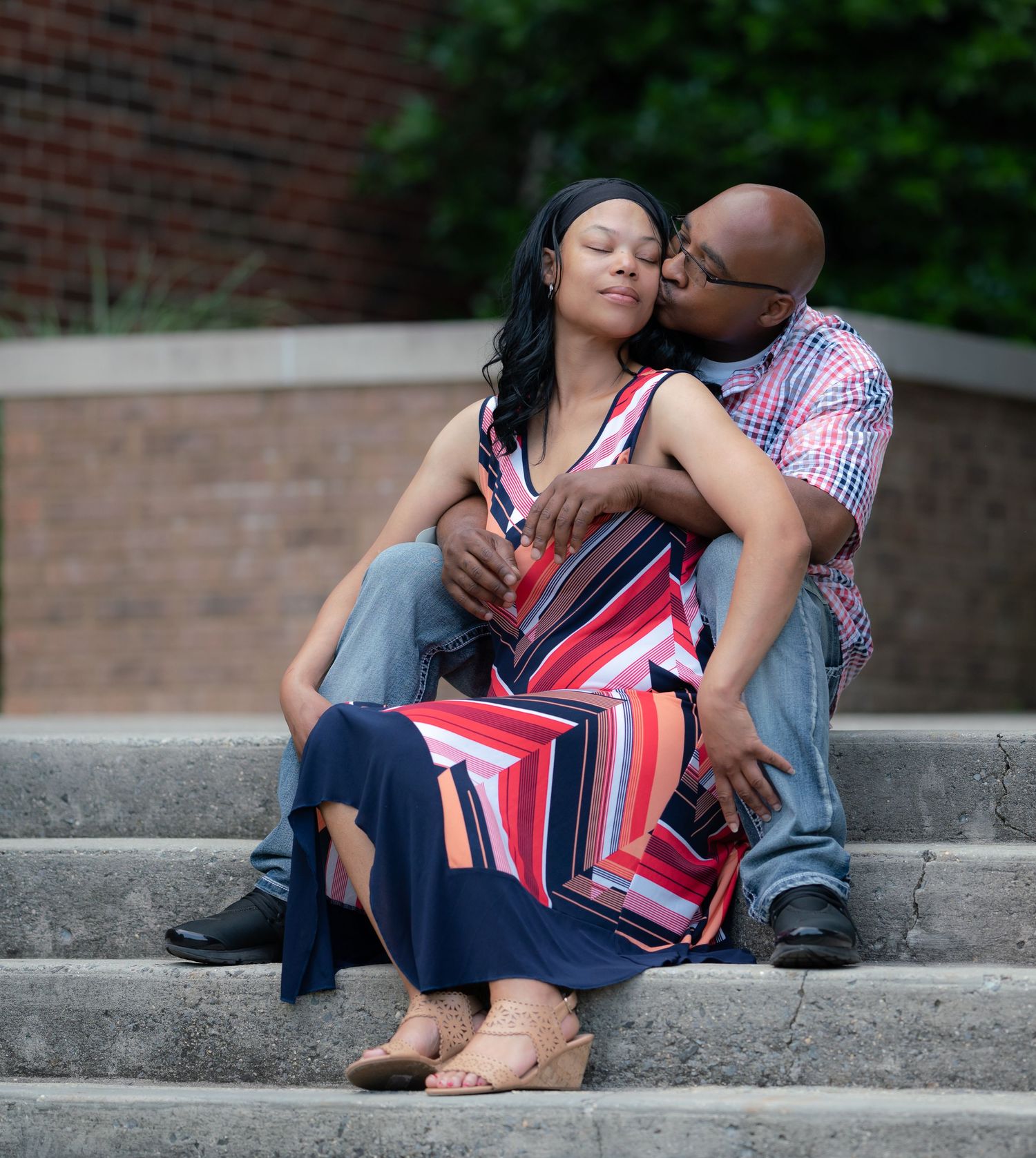 A couple in red and blue outfits sits together intimately on concrete steps outdoors.